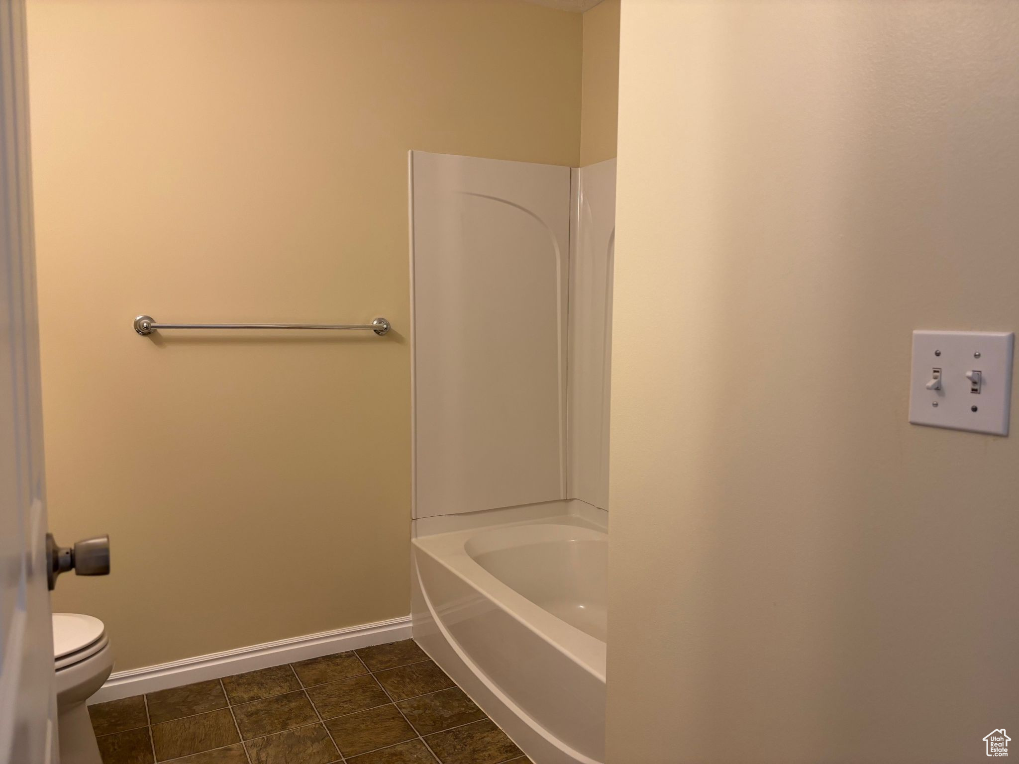 Full bathroom with toilet, a bathtub, baseboards, and tile-patterned flooring