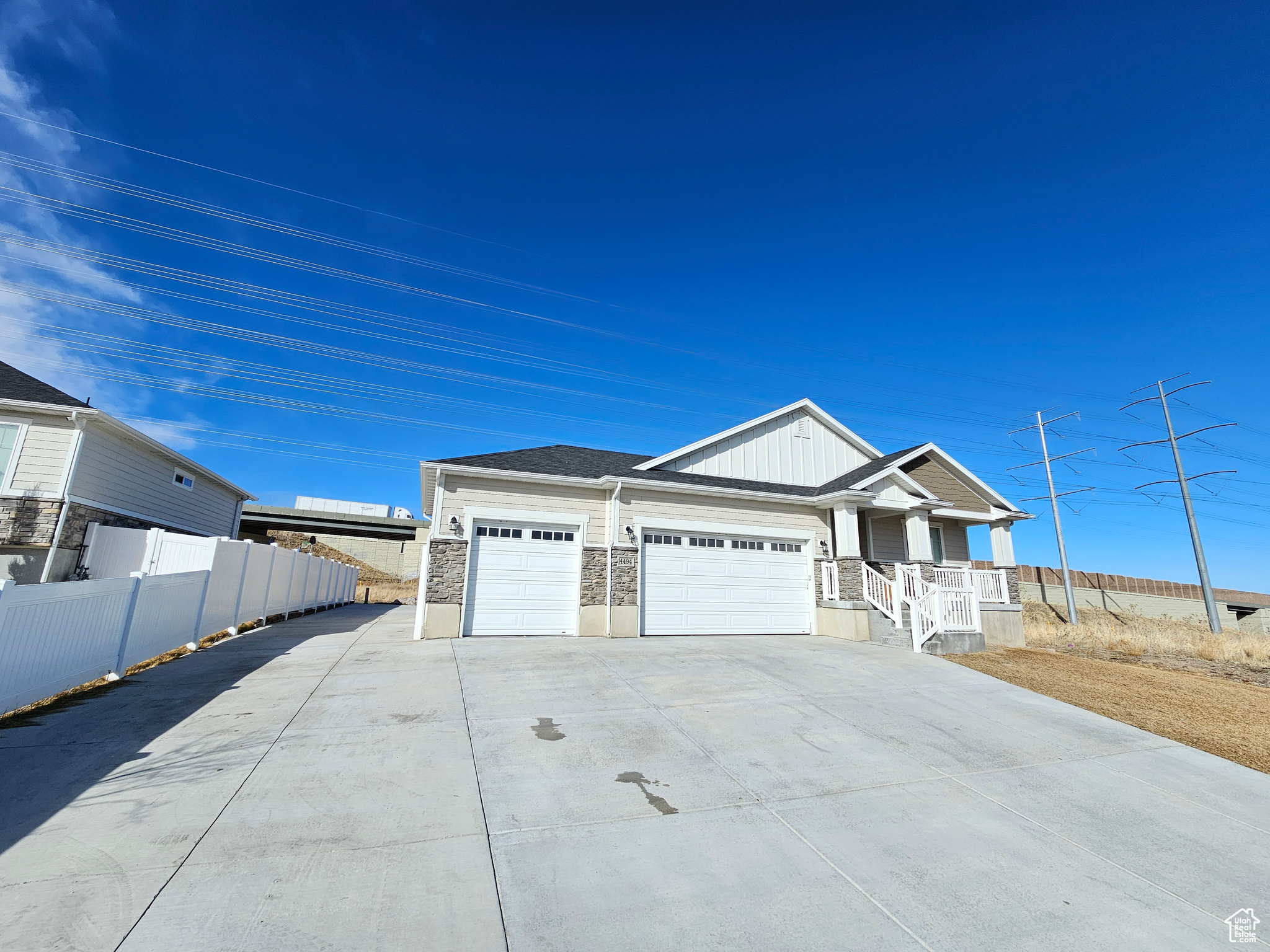 View of front facade with a porch, an attached garage, fence, driveway, and stone siding