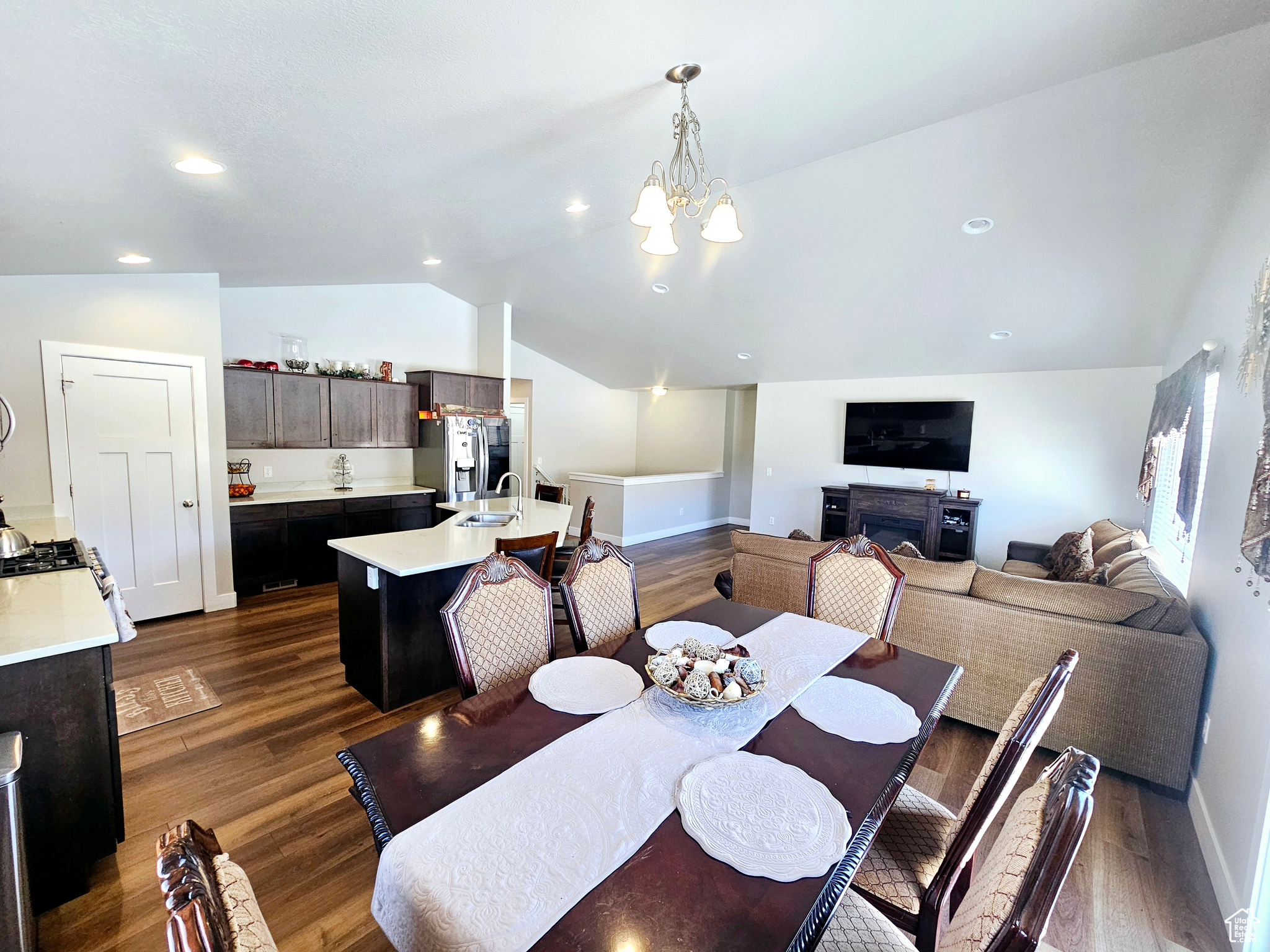 Dining area with dark wood-style flooring, a fireplace, a notable chandelier, lofted ceiling, and baseboards