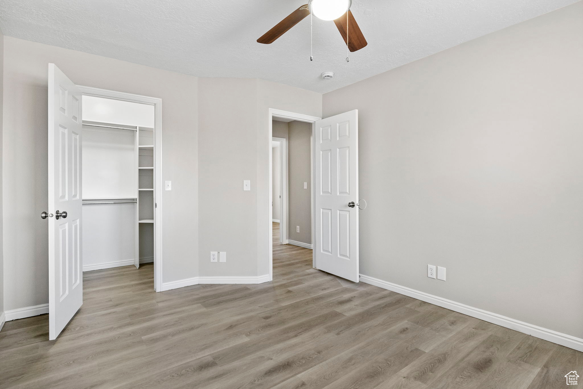 Unfurnished bedroom featuring baseboards, a ceiling fan, a walk in closet, light wood-type flooring, and a closet