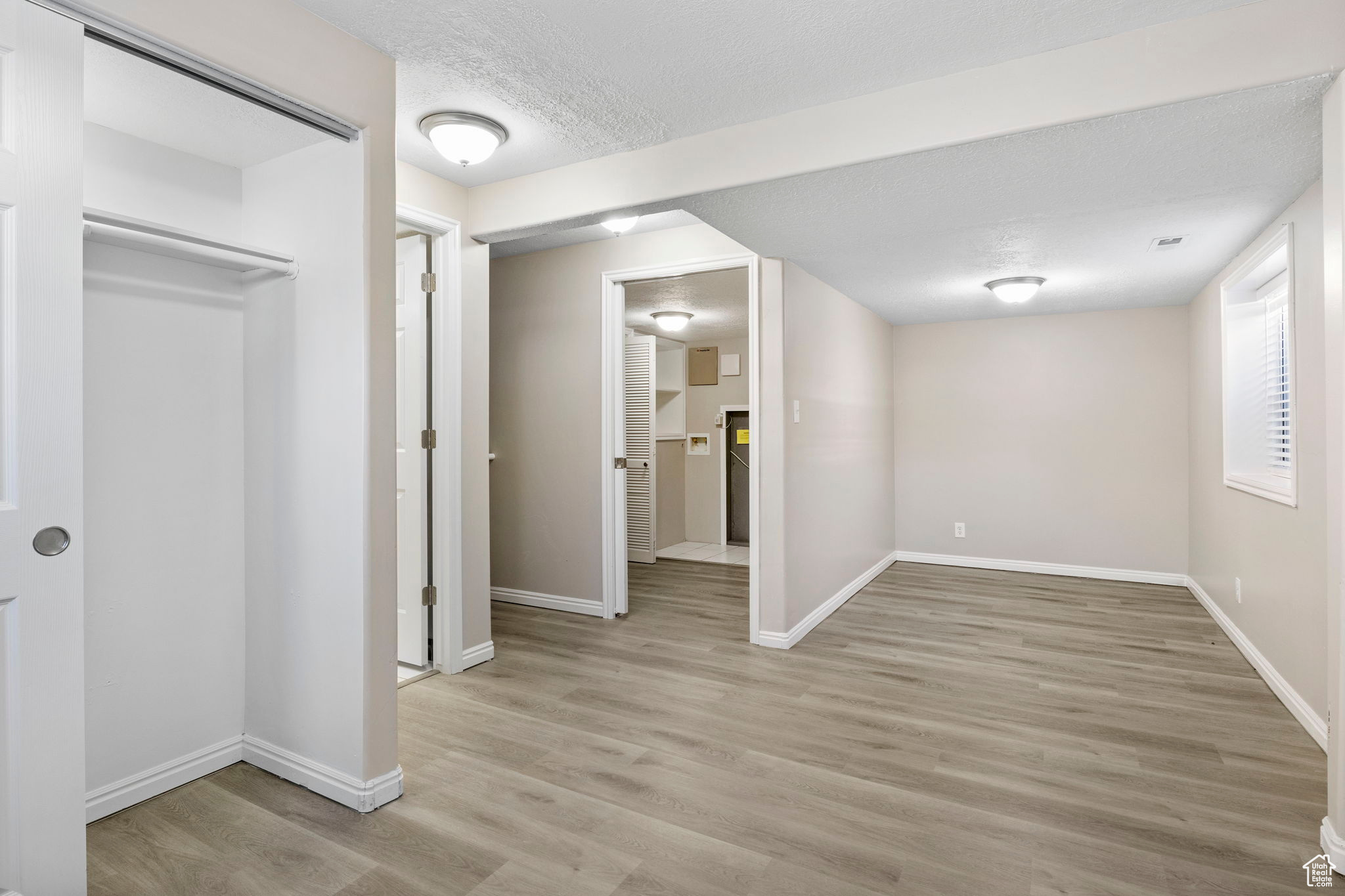 Below grade area featuring a textured ceiling, light wood-type flooring, and baseboards