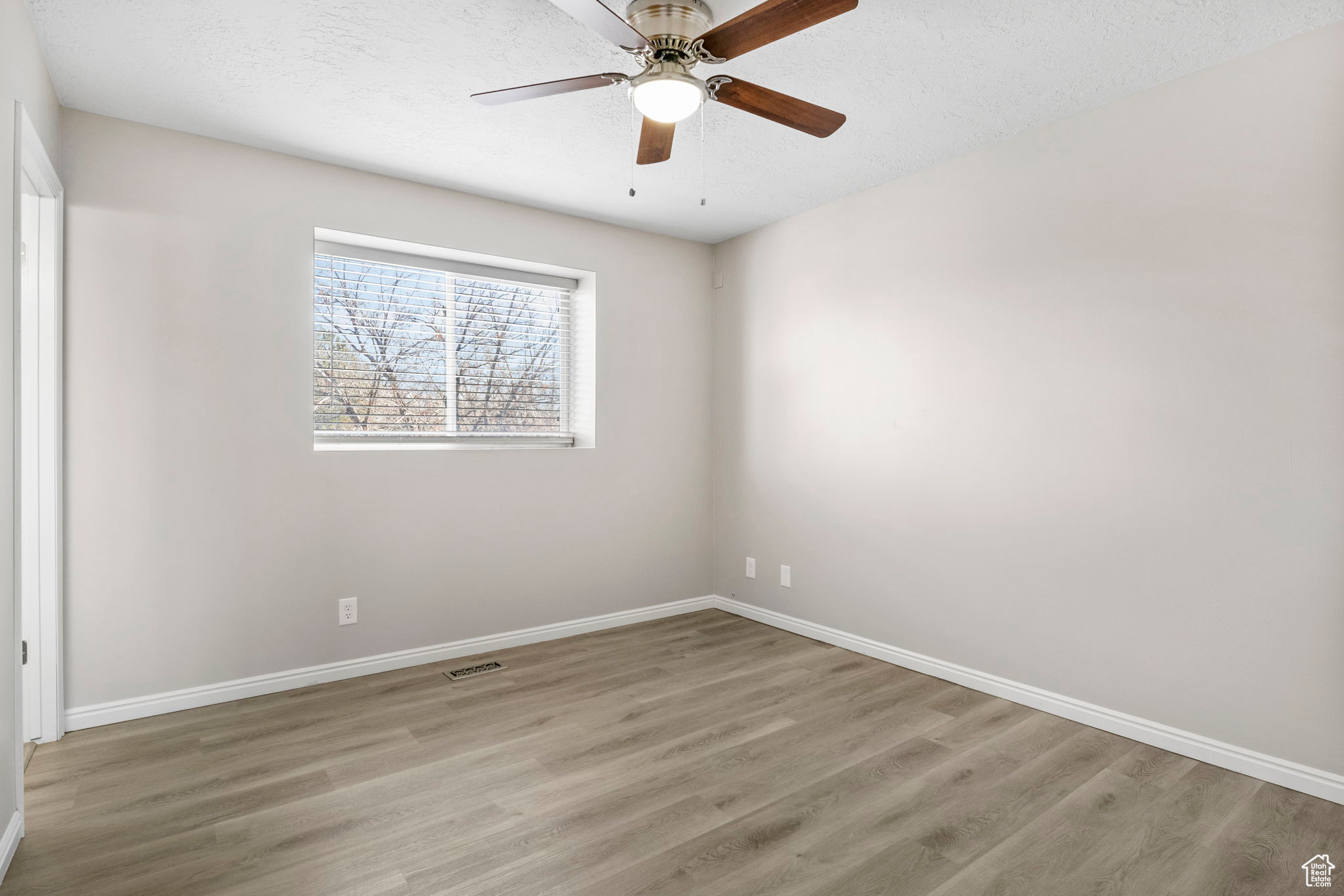 Unfurnished room featuring baseboards, visible vents, a ceiling fan, wood finished floors, and a textured ceiling