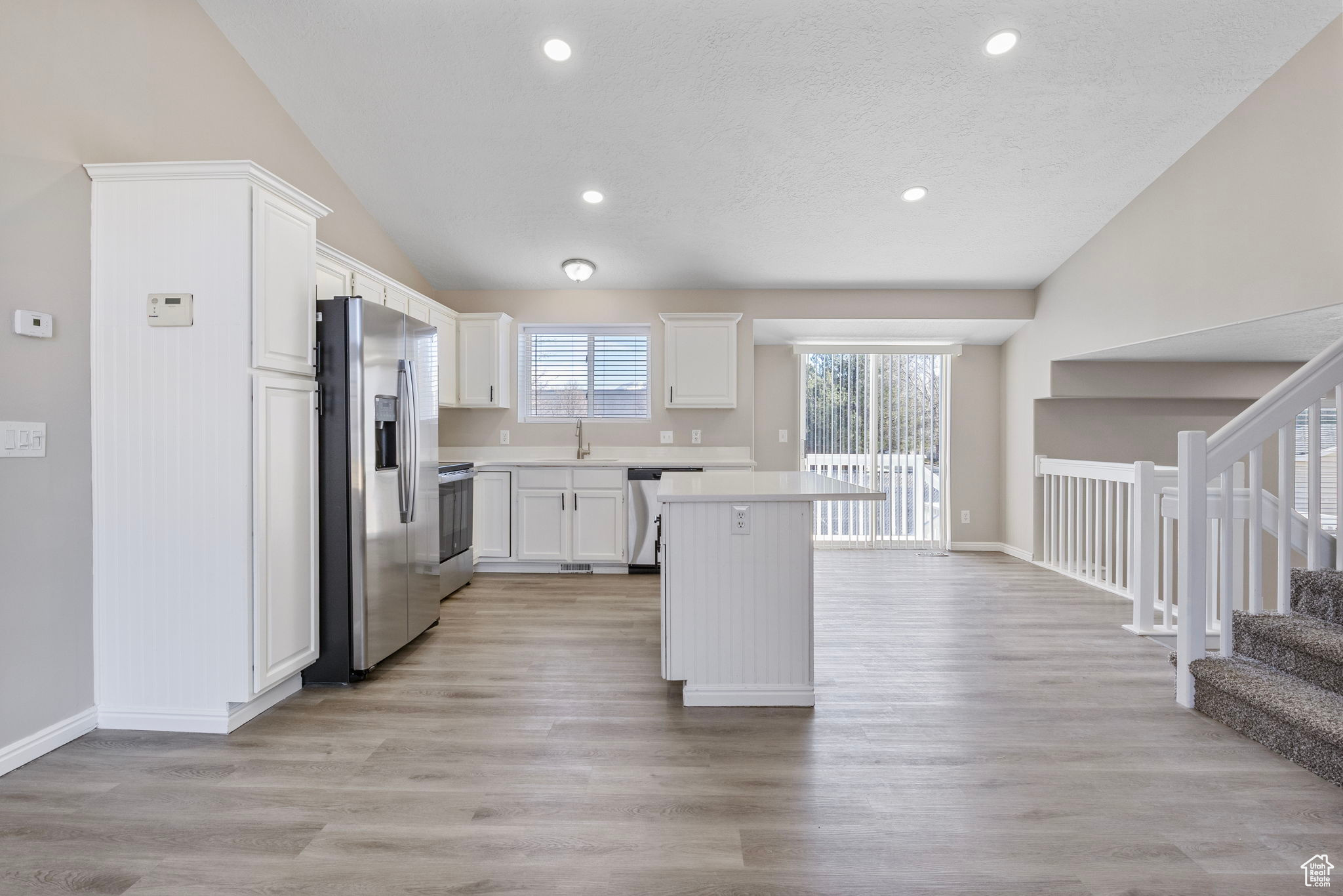 Kitchen with appliances with stainless steel finishes, open floor plan, light countertops, white cabinetry, and a sink