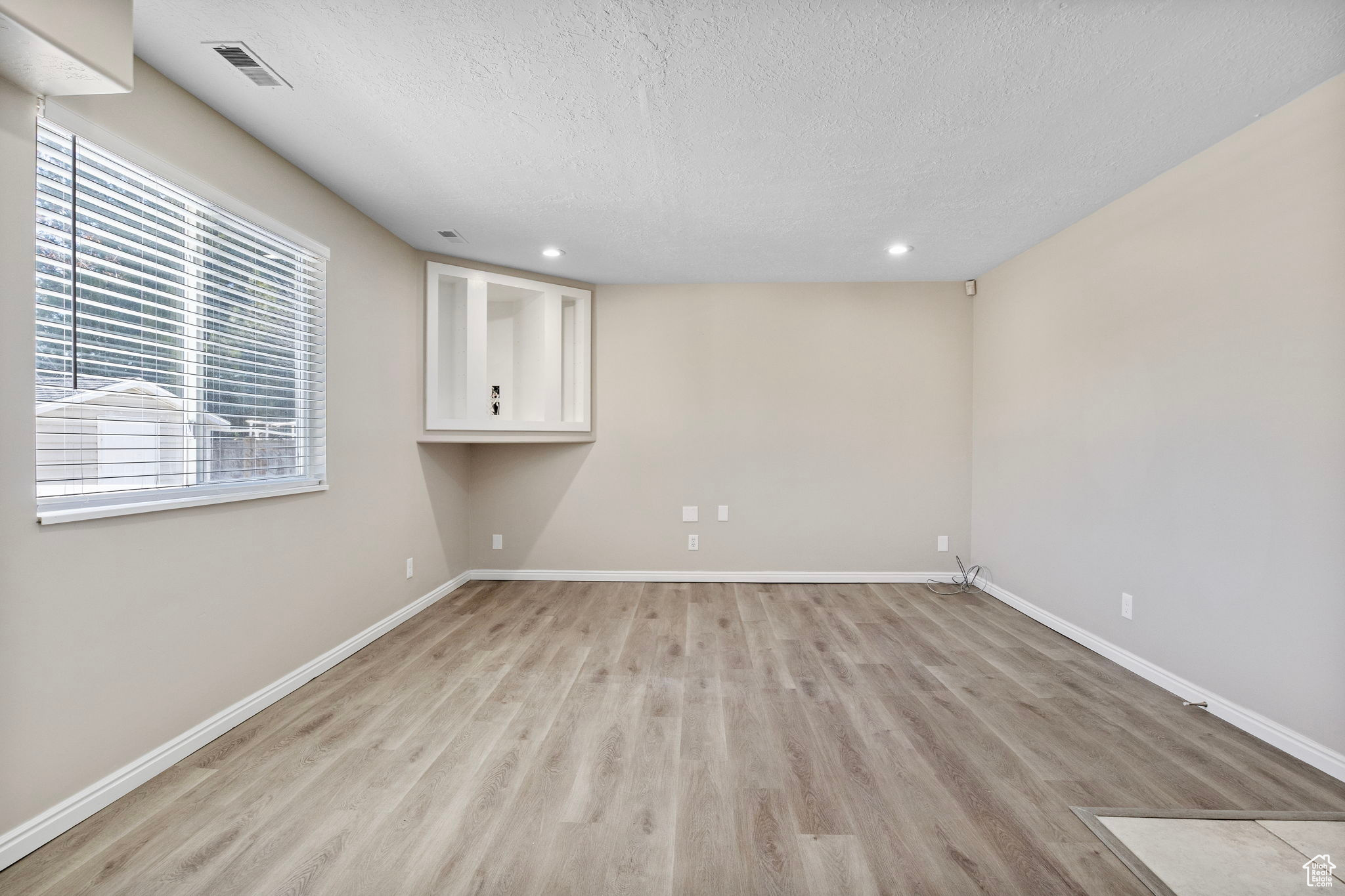 Spare room with a textured ceiling, light wood finished floors, visible vents, and baseboards