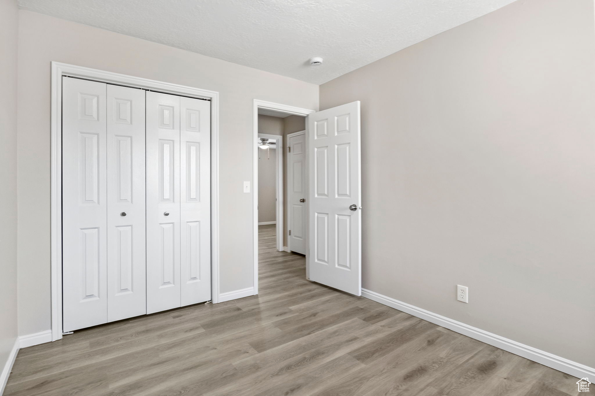 Unfurnished bedroom featuring light wood-type flooring, a closet, a textured ceiling, and baseboards