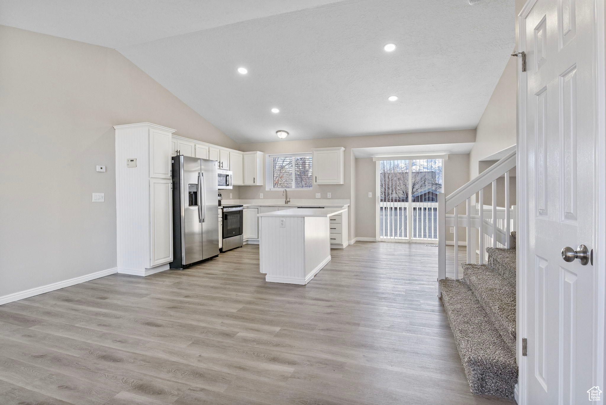 Kitchen featuring white cabinets, open floor plan, light countertops, appliances with stainless steel finishes, and a center island