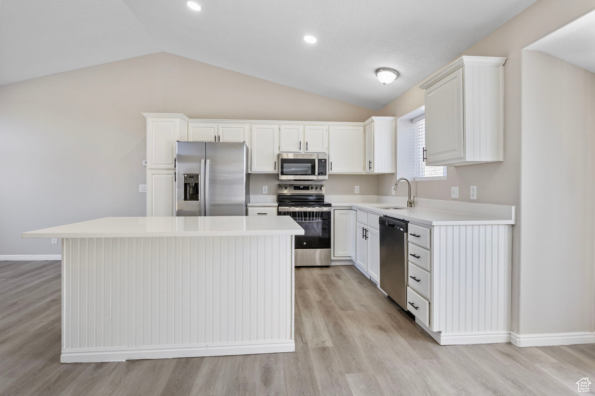 Kitchen featuring white cabinets, a kitchen island, stainless steel appliances, light countertops, and a sink