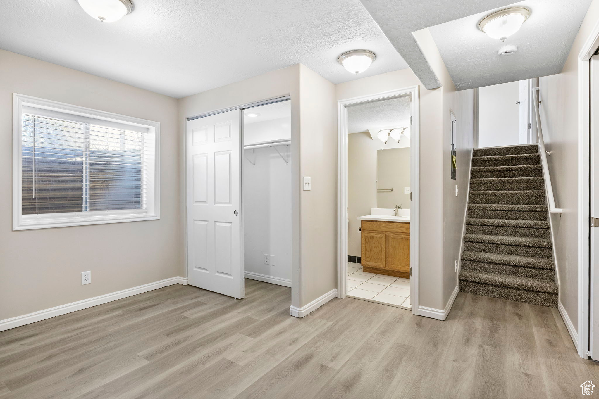 Unfurnished bedroom featuring light wood finished floors, a closet, connected bathroom, and baseboards
