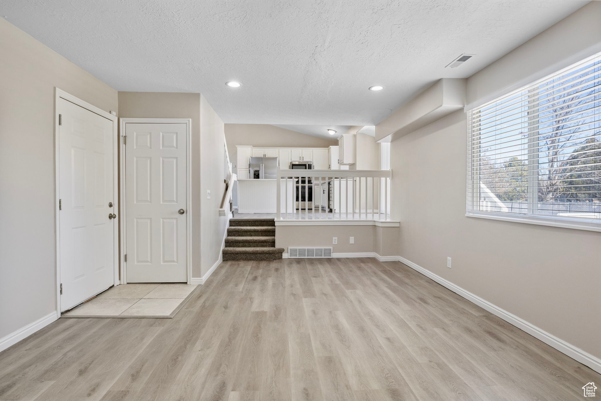 Unfurnished room with a textured ceiling, visible vents, baseboards, stairs, and light wood finished floors