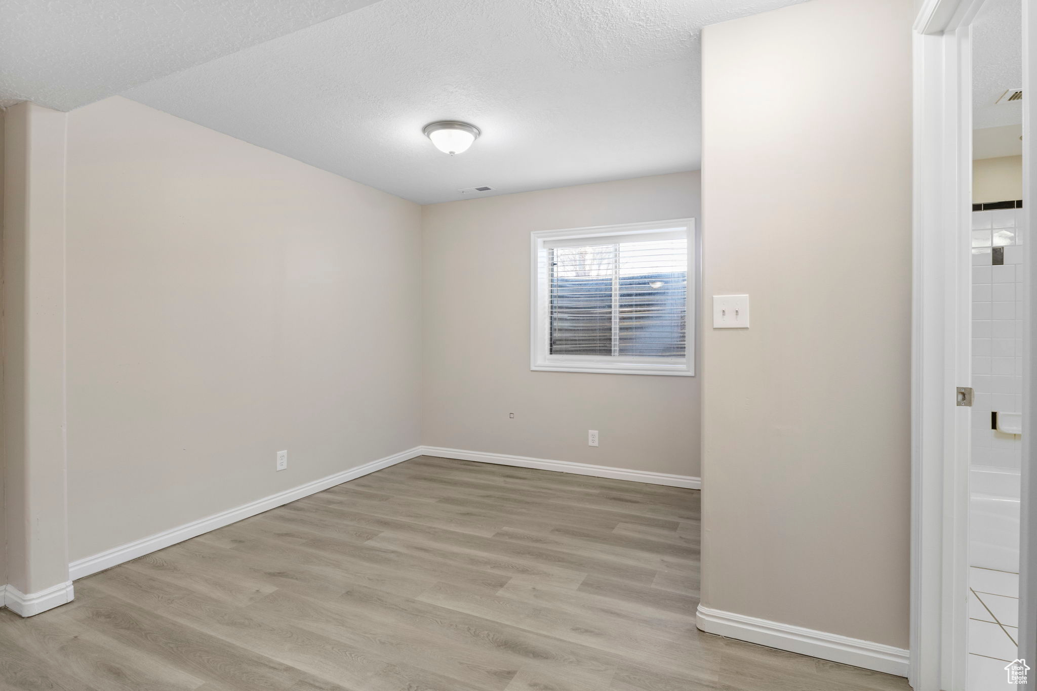 Empty room with light wood-style floors, visible vents, and baseboards