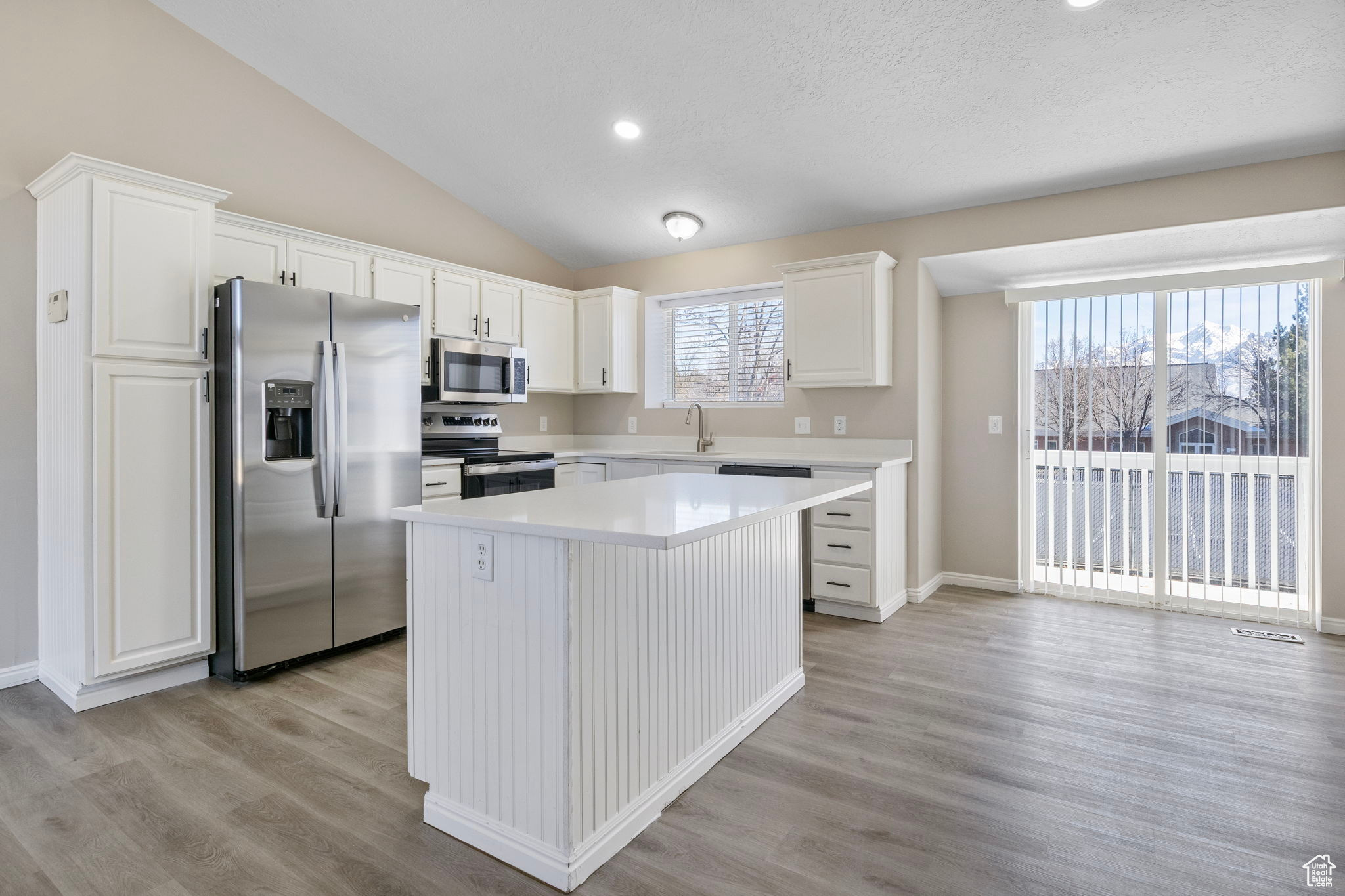 Kitchen featuring stainless steel appliances, light countertops, white cabinetry, a kitchen island, and a sink