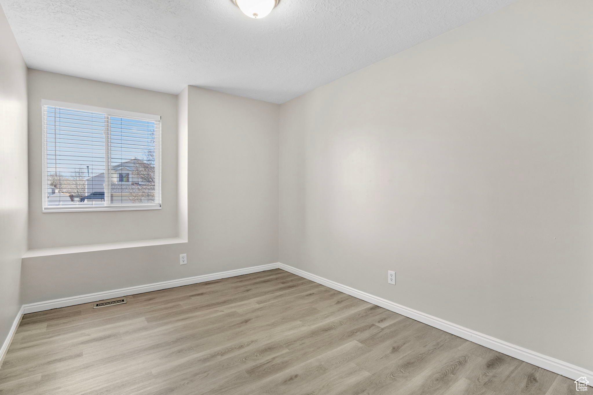 Empty room featuring visible vents, light wood-style flooring, baseboards, and a textured ceiling