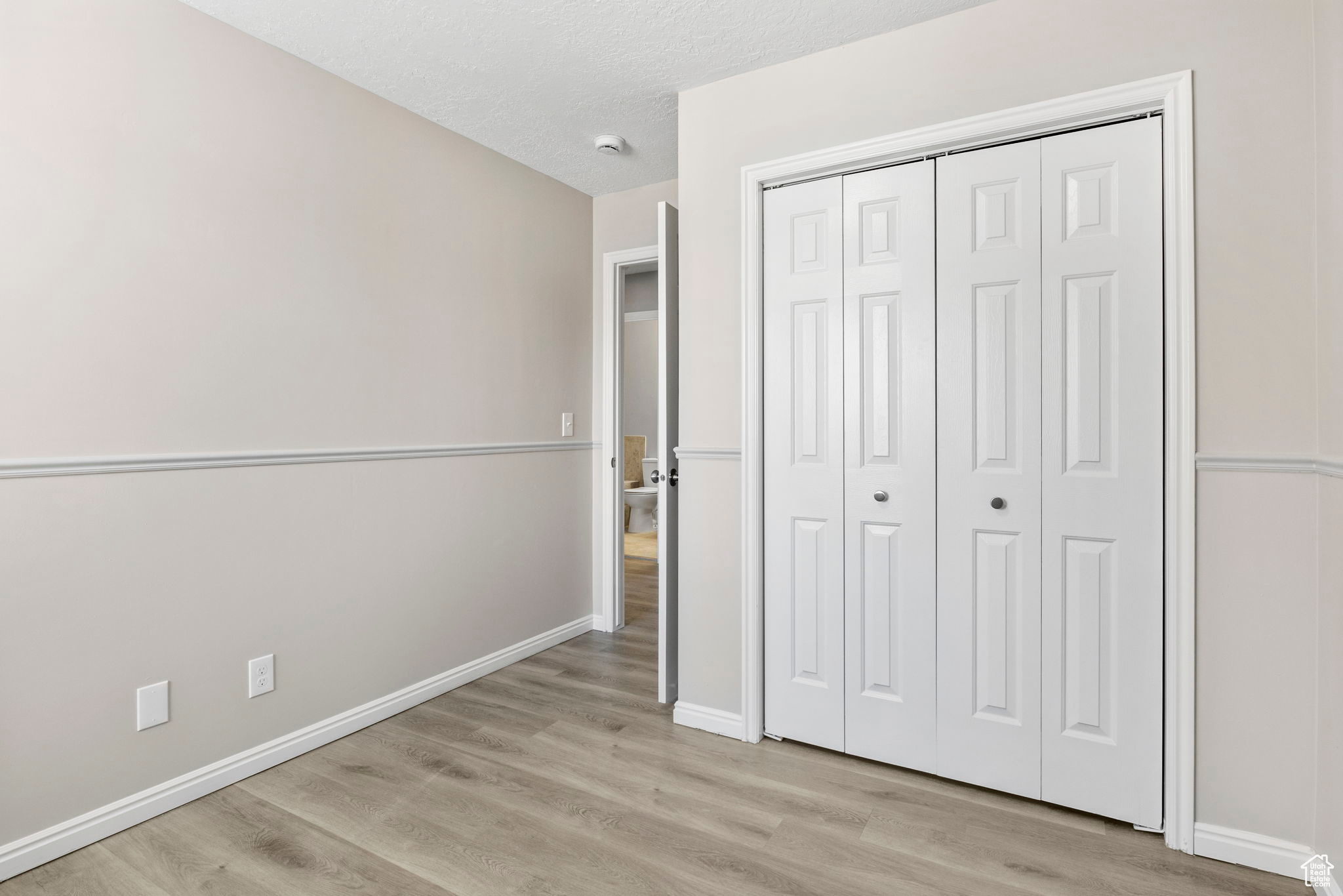Unfurnished bedroom featuring a textured ceiling, a closet, light wood-style flooring, and baseboards