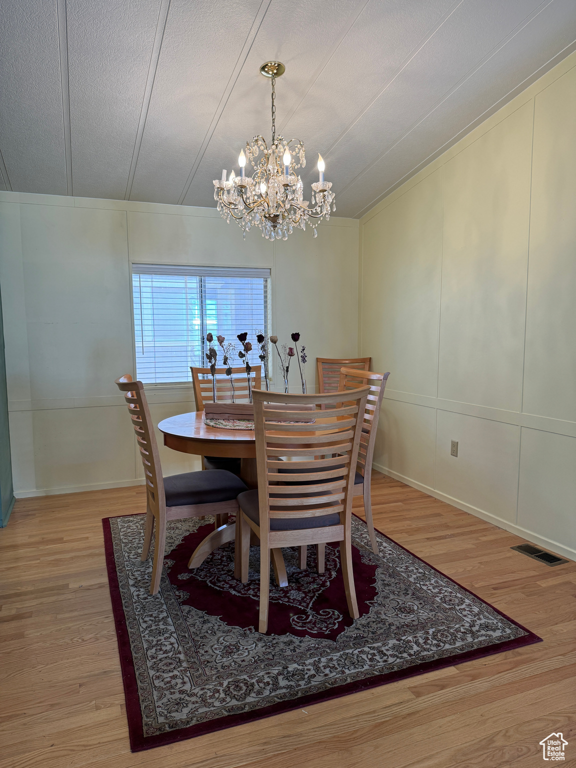 Dining area featuring a notable chandelier, light wood finished floors, visible vents, a decorative wall, and a textured ceiling