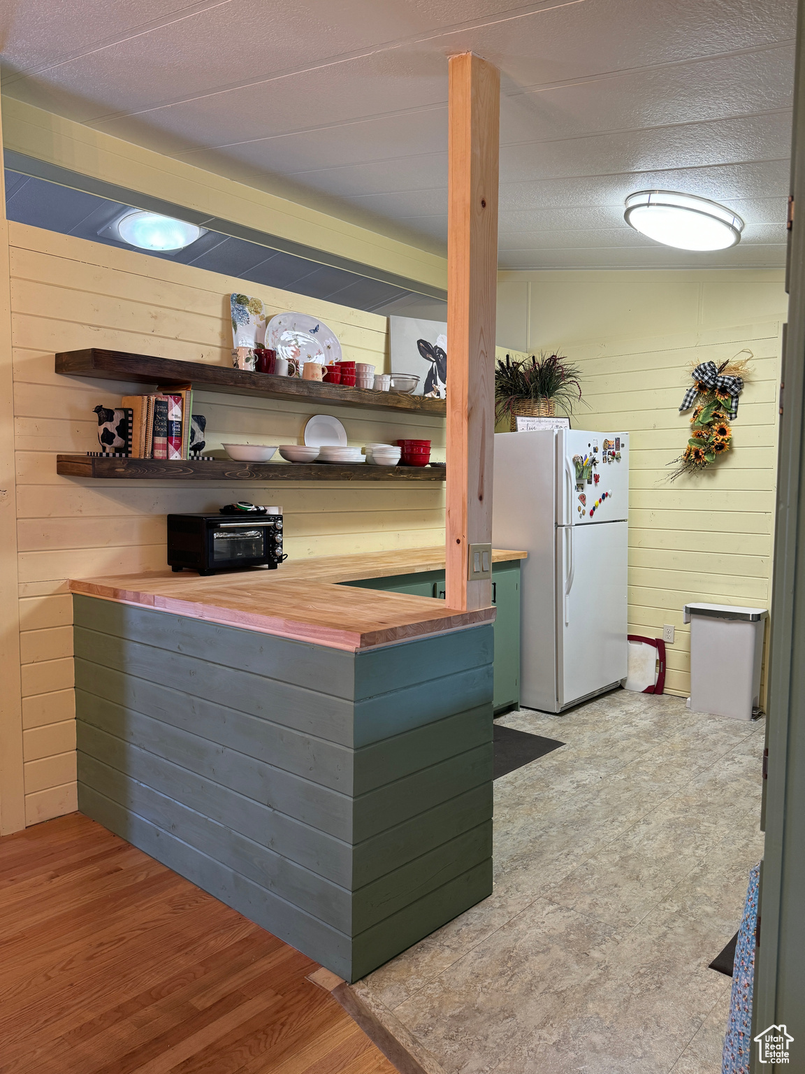 Kitchen with open shelves, wood walls, light wood-type flooring, and freestanding refrigerator
