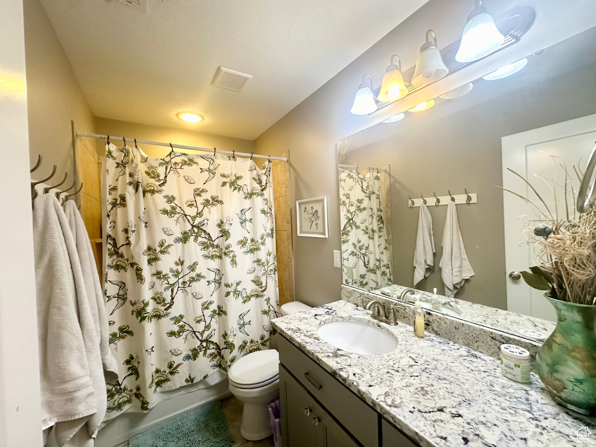 Full bathroom with shower / bath combination with curtain, visible vents, vanity, and toilet