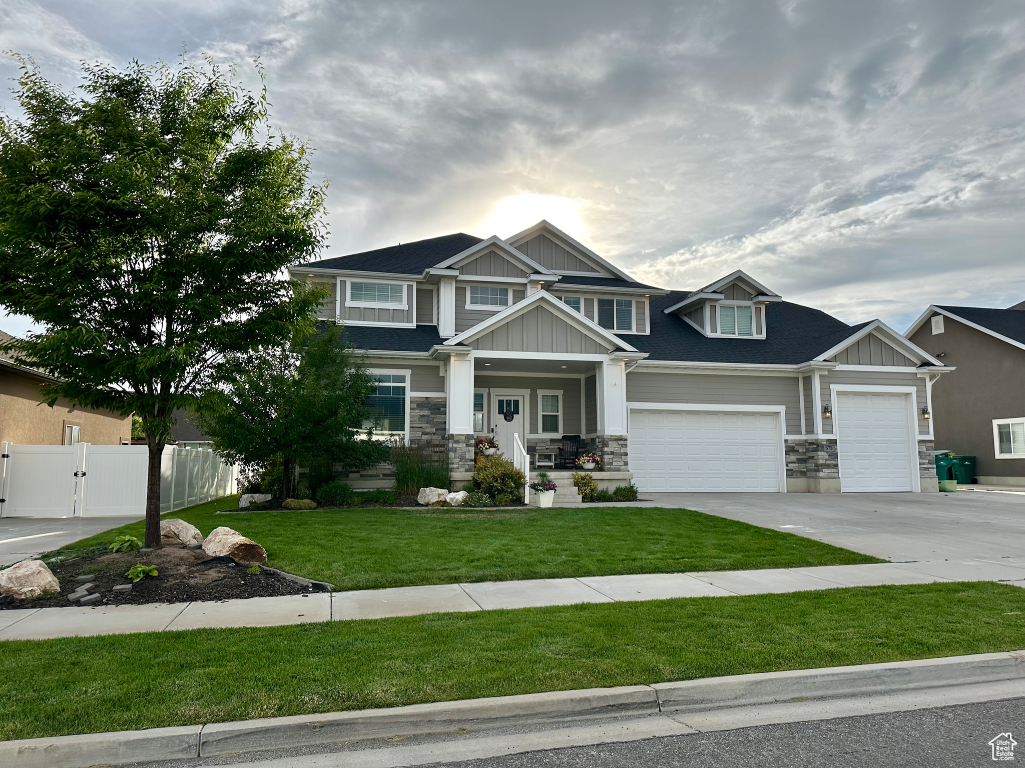 Craftsman-style house featuring concrete driveway, stone siding, a gate, fence, and board and batten siding