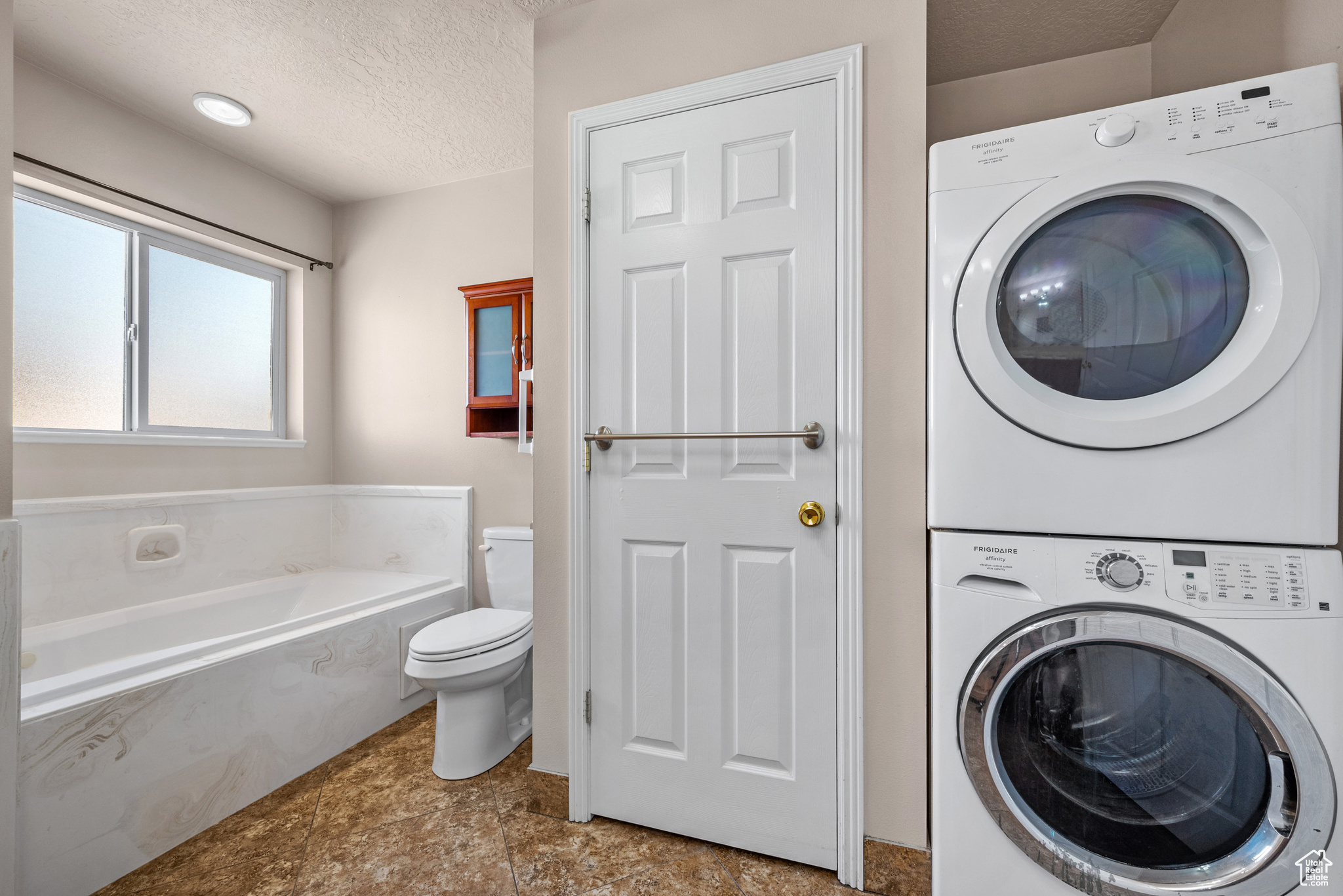 Laundry room featuring a textured ceiling, laundry area, and stacked washing maching and dryer