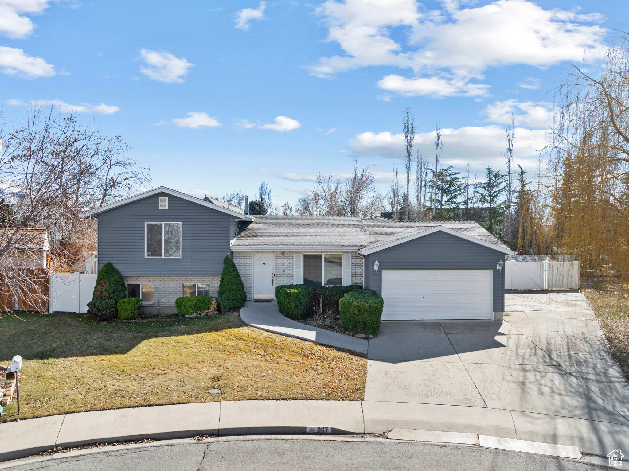 Split level home with brick siding, driveway, an attached garage, and fence
