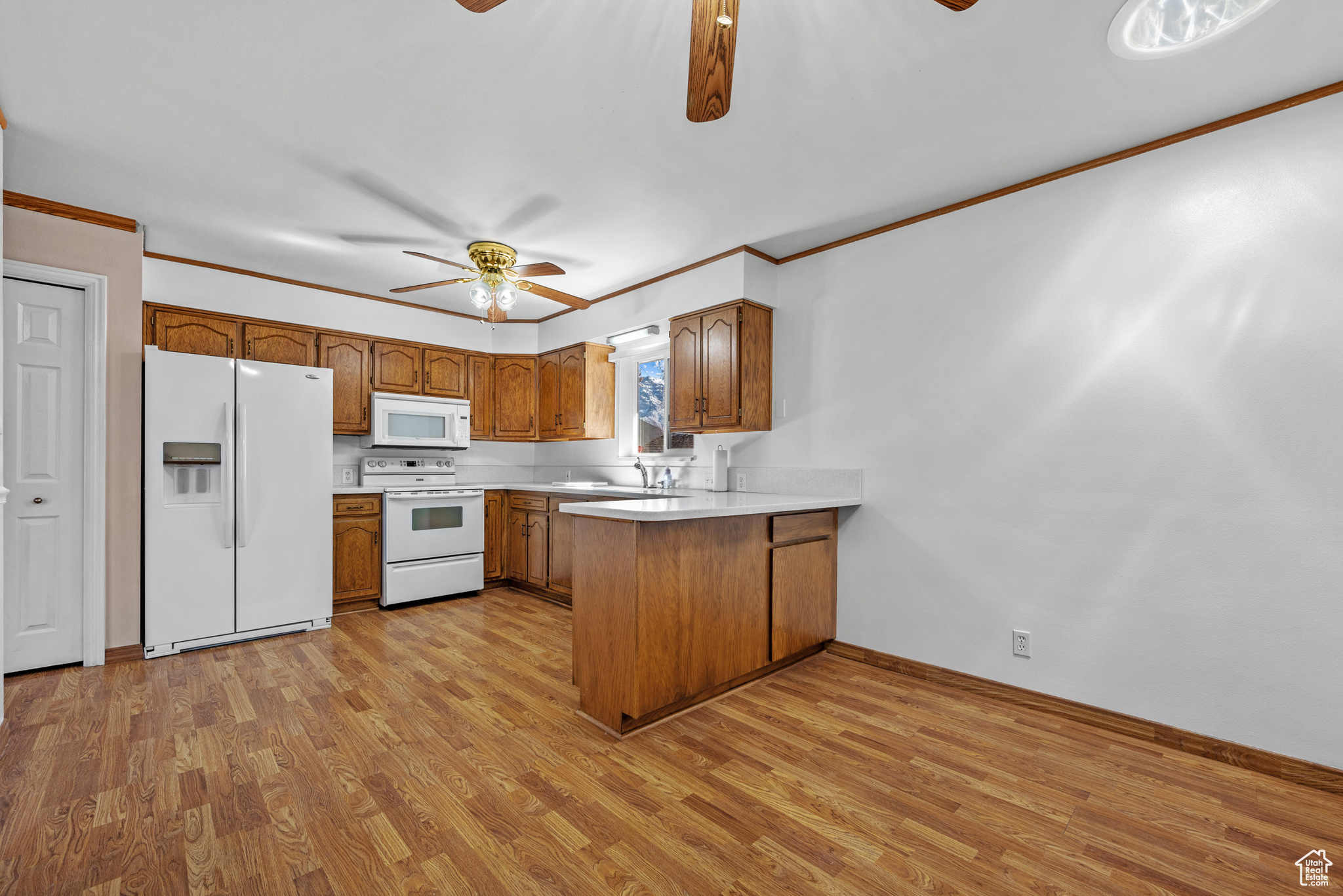 Kitchen featuring light countertops, brown cabinetry, a ceiling fan, white appliances, and a peninsula