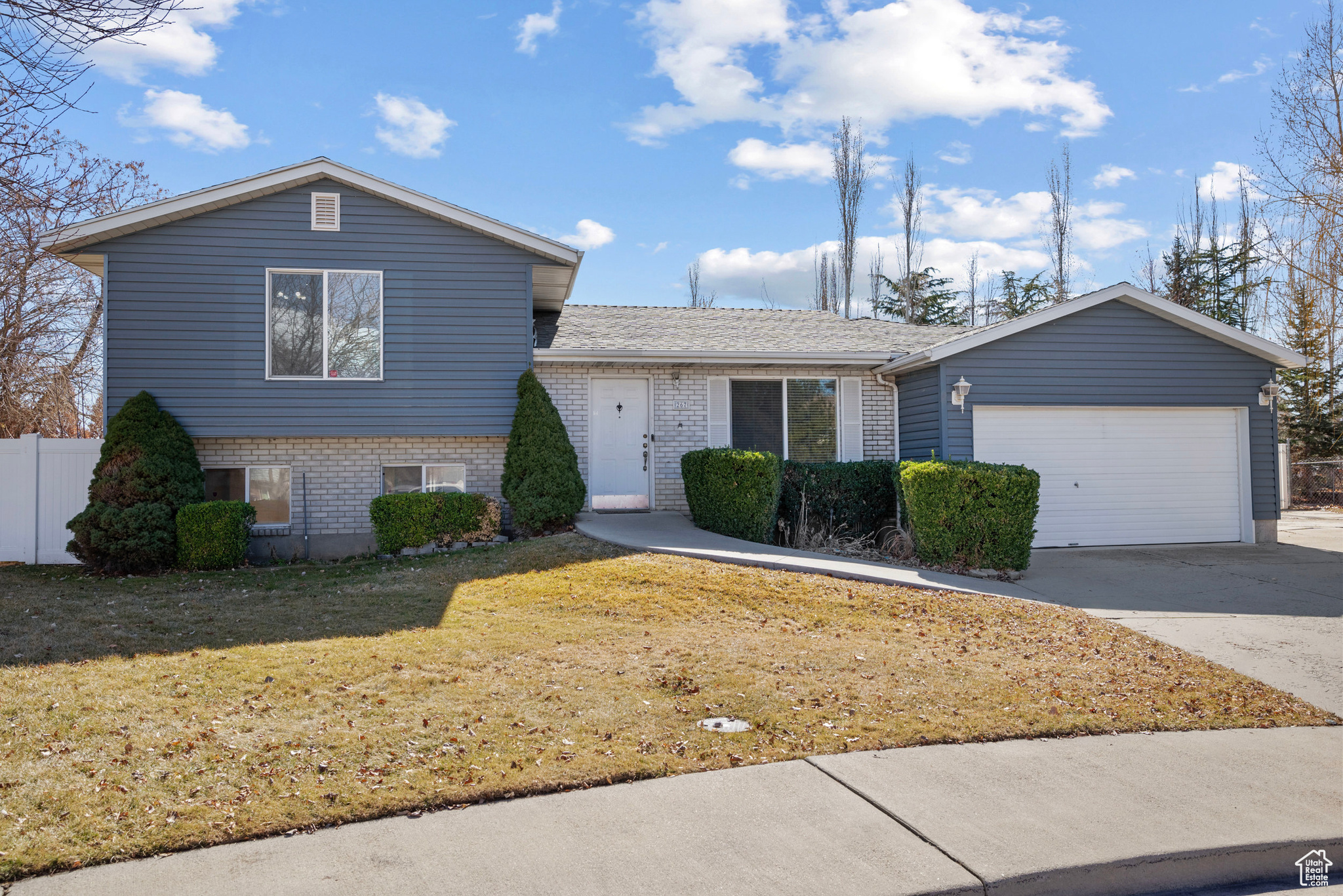 Tri-level home with brick siding, an attached garage, a front yard, fence, and driveway