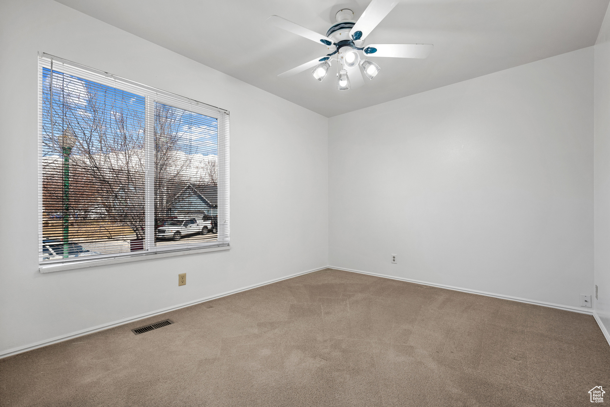 Carpeted empty room featuring a ceiling fan, visible vents, and baseboards