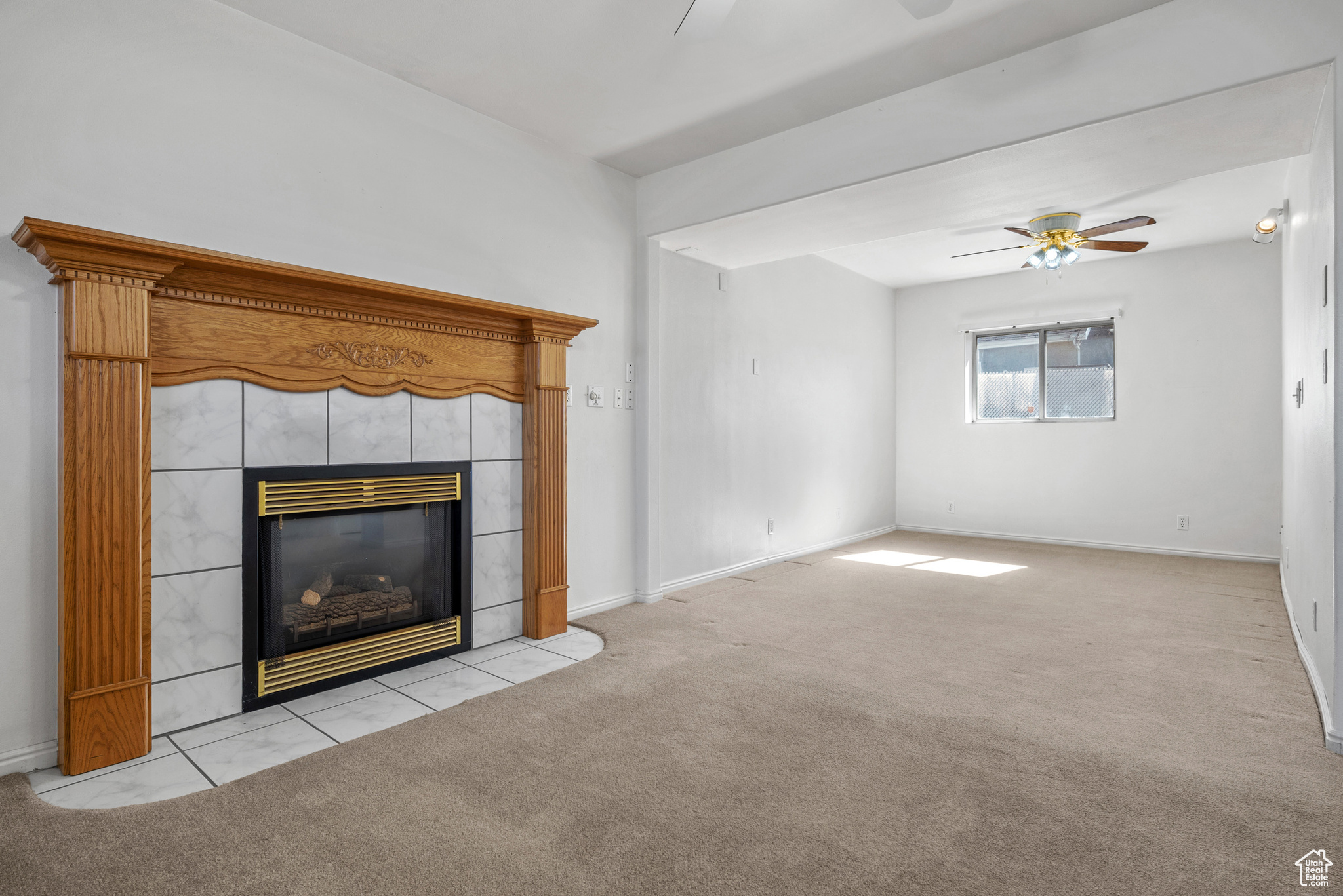 Unfurnished living room with baseboards, light colored carpet, ceiling fan, and a tiled fireplace