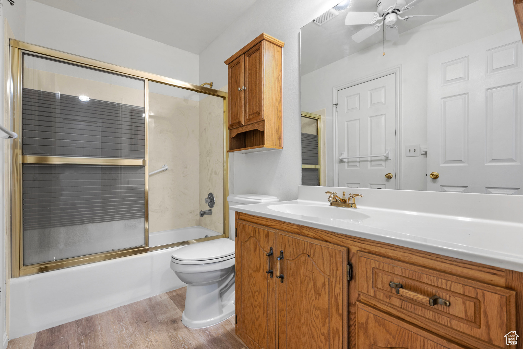 Bathroom featuring enclosed tub / shower combo, ceiling fan, toilet, wood finished floors, and vanity