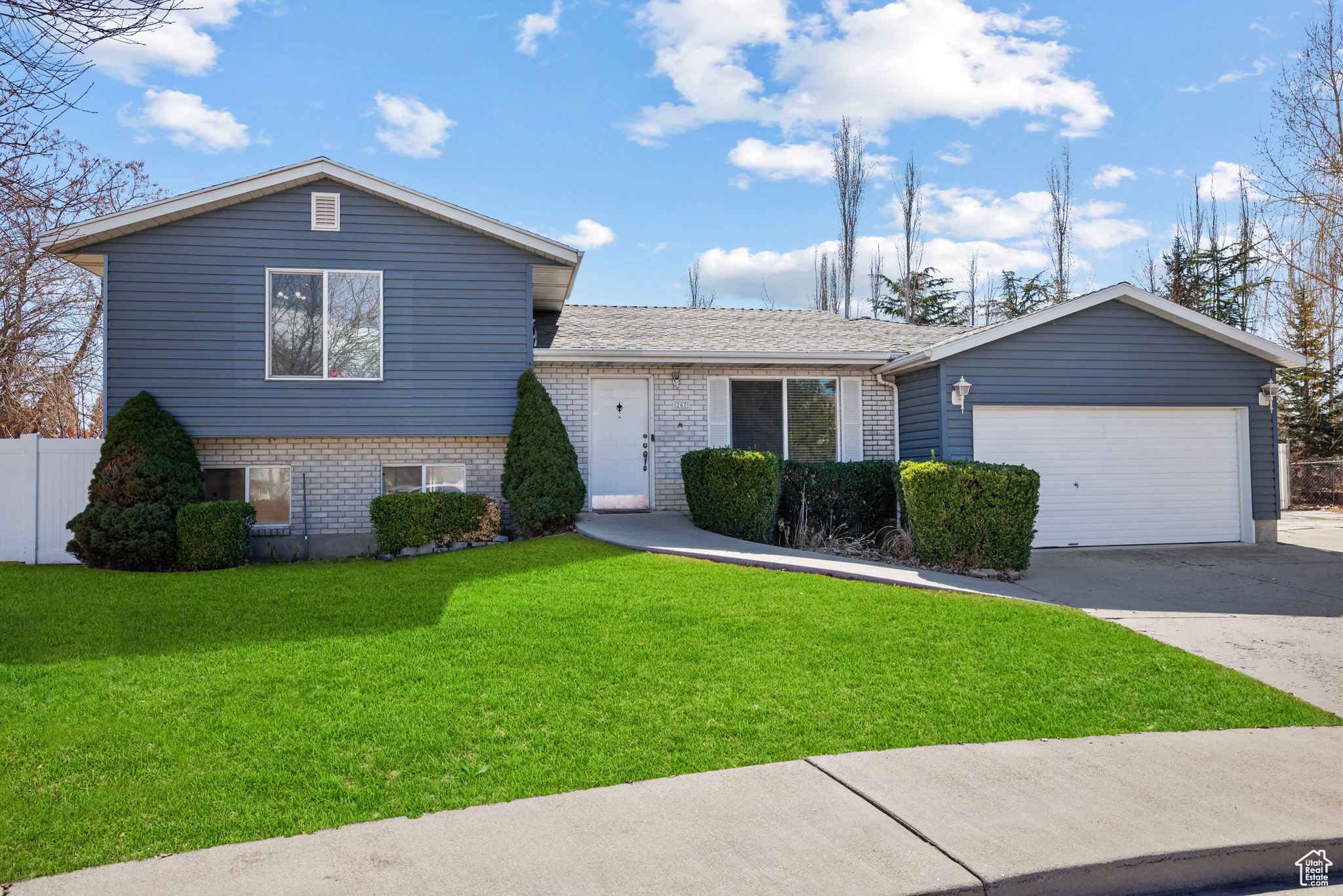 Split level home featuring brick siding, concrete driveway, an attached garage, fence, and a front lawn