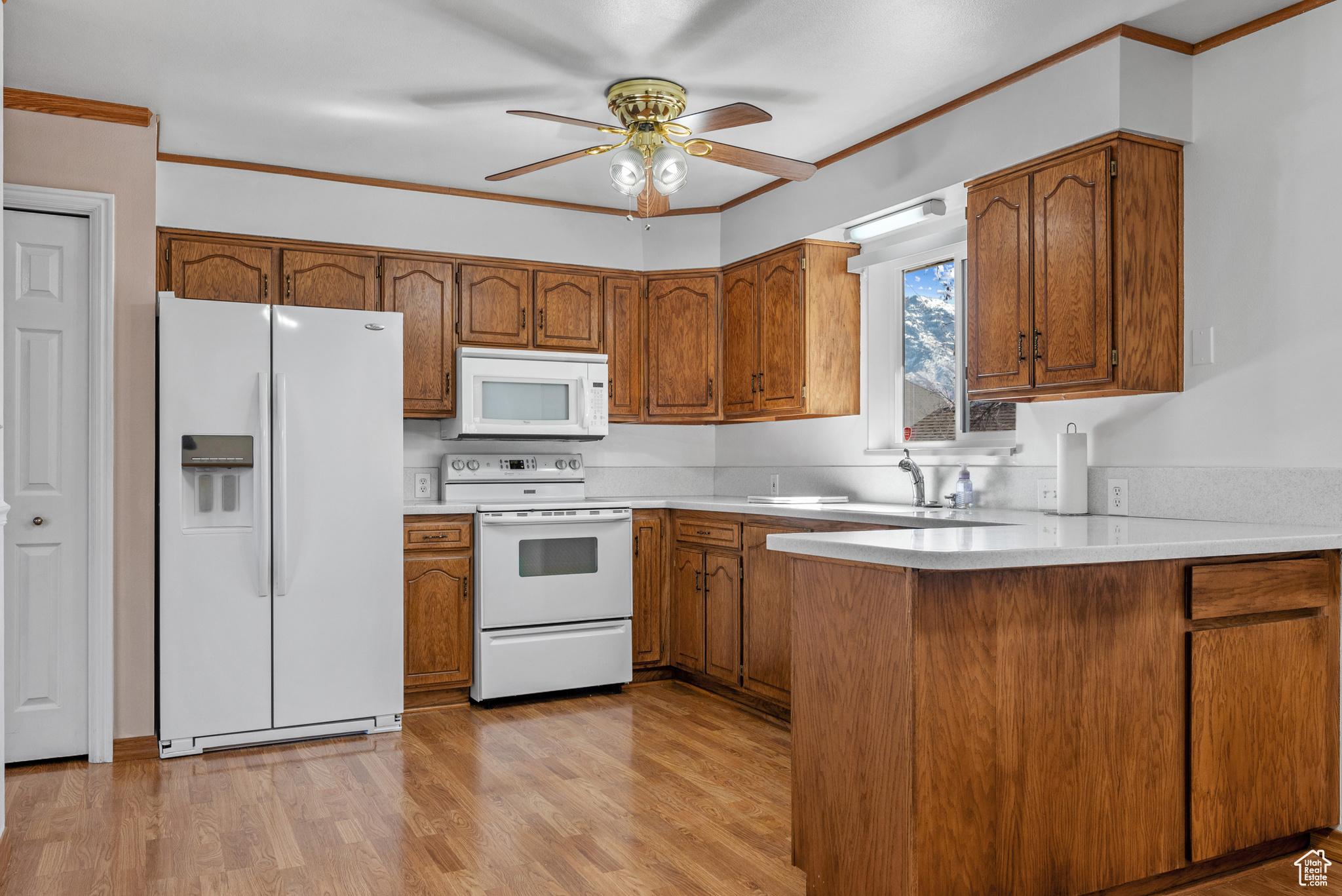 Kitchen featuring light countertops, white appliances, brown cabinetry, and a sink
