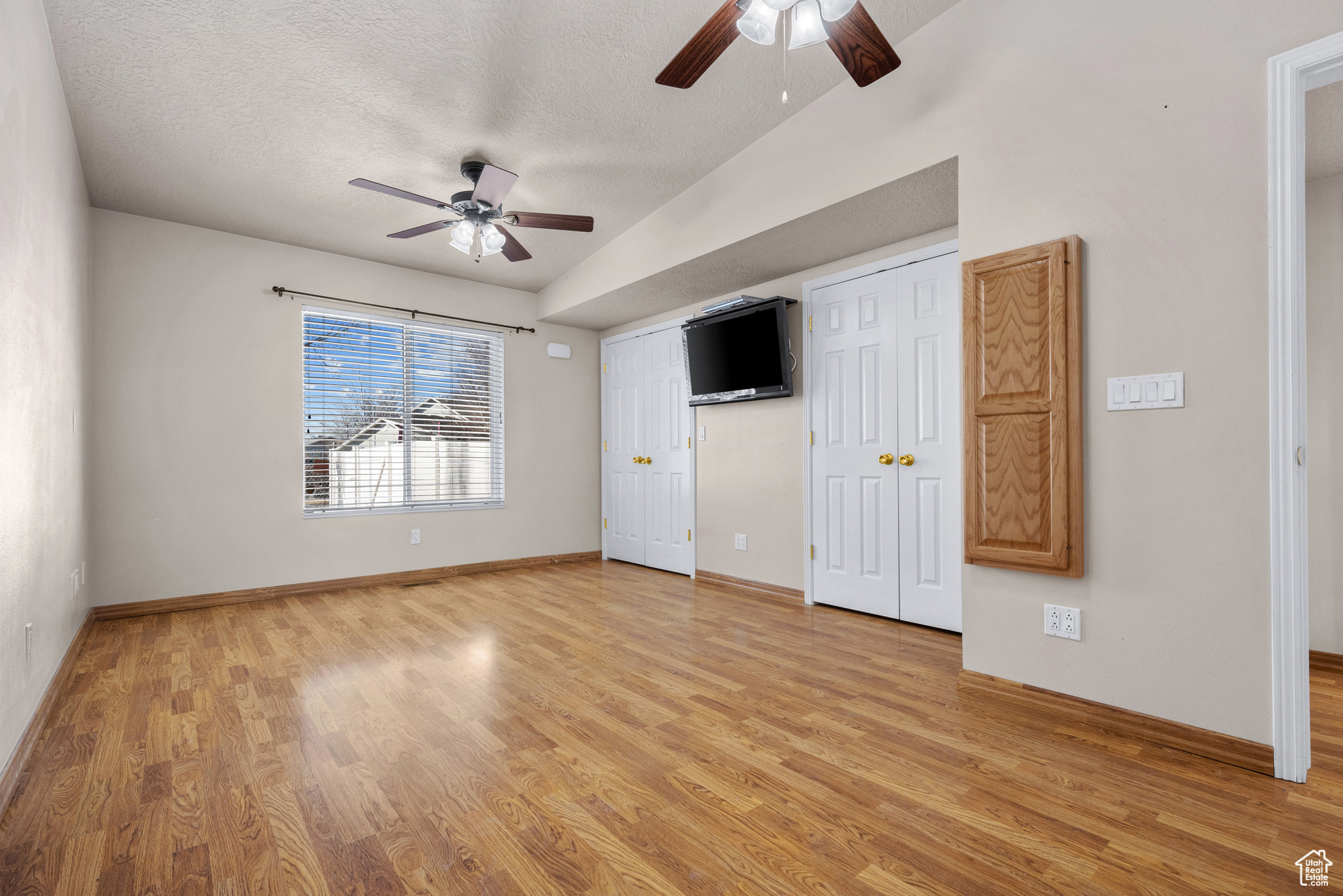 Unfurnished bedroom featuring baseboards, a ceiling fan, a textured ceiling, light wood-type flooring, and two closets