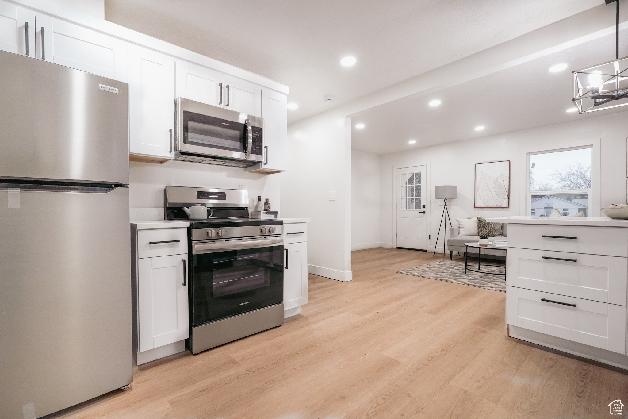 Kitchen featuring stainless steel appliances, hanging light fixtures, light countertops, and white cabinetry