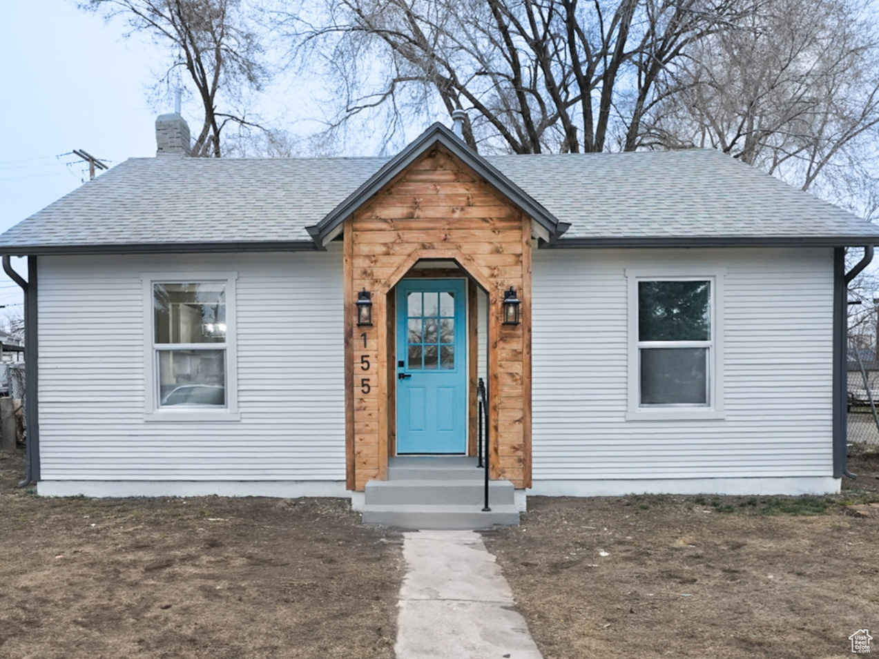 Bungalow-style home featuring a shingled roof, entry steps, fence, and a chimney