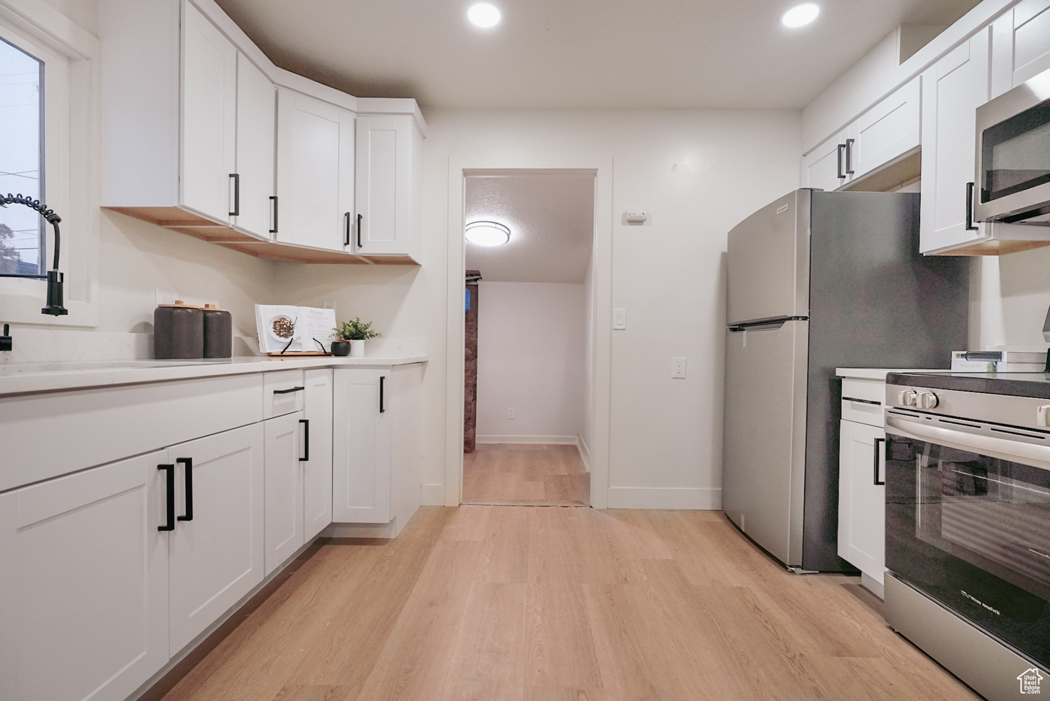 Kitchen with light wood finished floors, recessed lighting, light countertops, appliances with stainless steel finishes, and white cabinetry