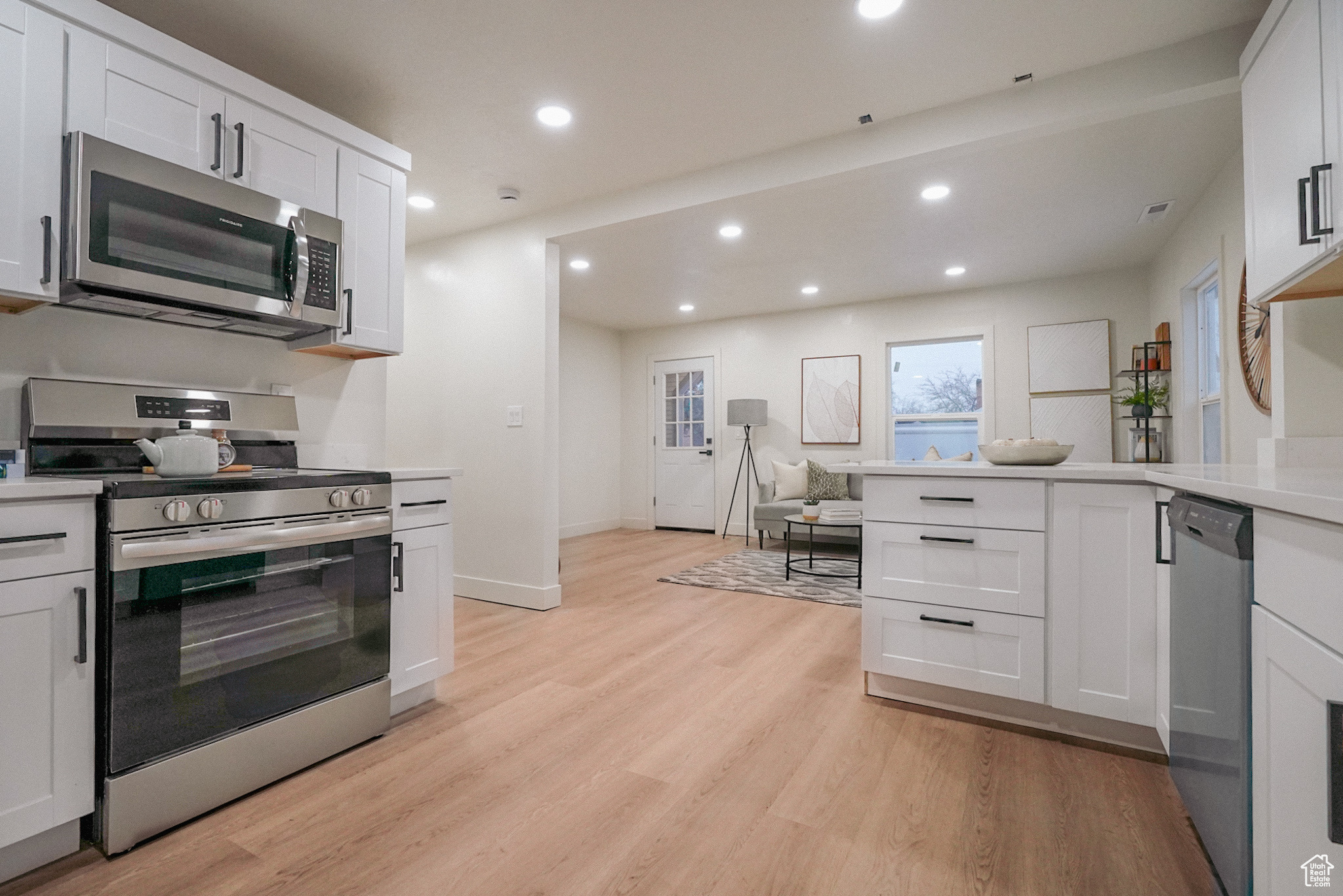 Kitchen with white cabinets, appliances with stainless steel finishes, light countertops, light wood-type flooring, and recessed lighting
