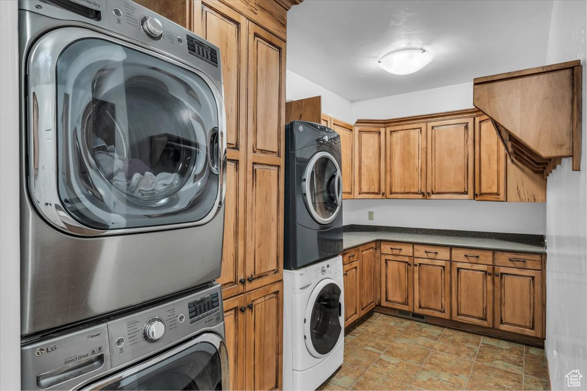 Clothes washing area featuring stacked washing maching and dryer and cabinet space