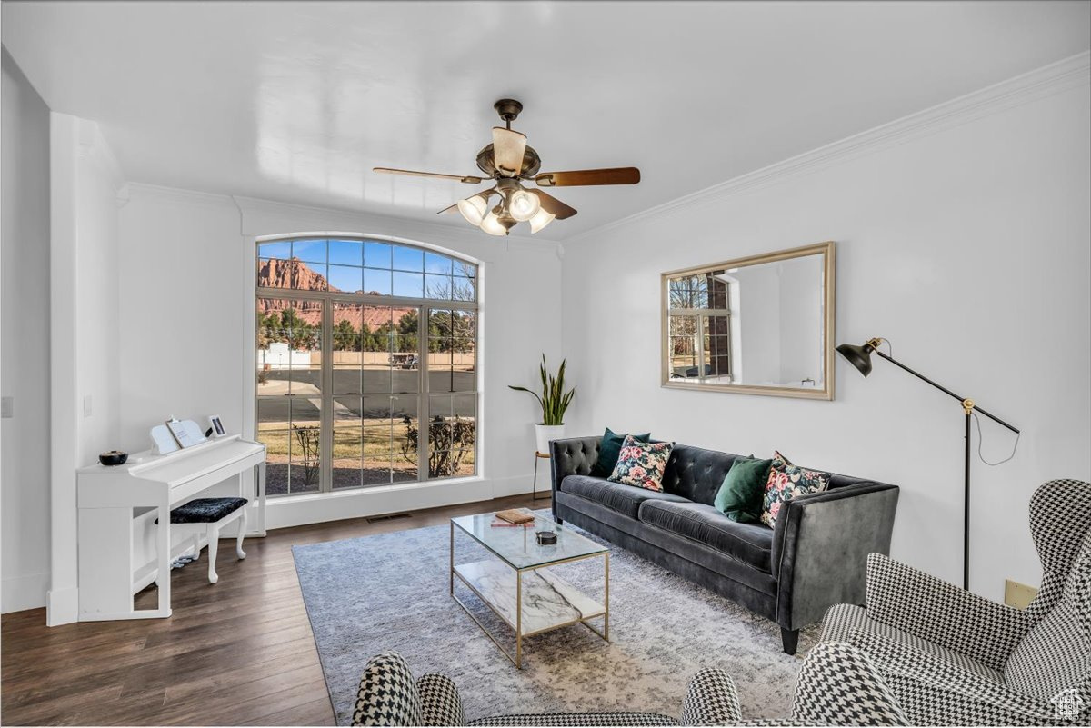 Living room with dark wood-style flooring, visible vents, a ceiling fan, baseboards, and ornamental molding