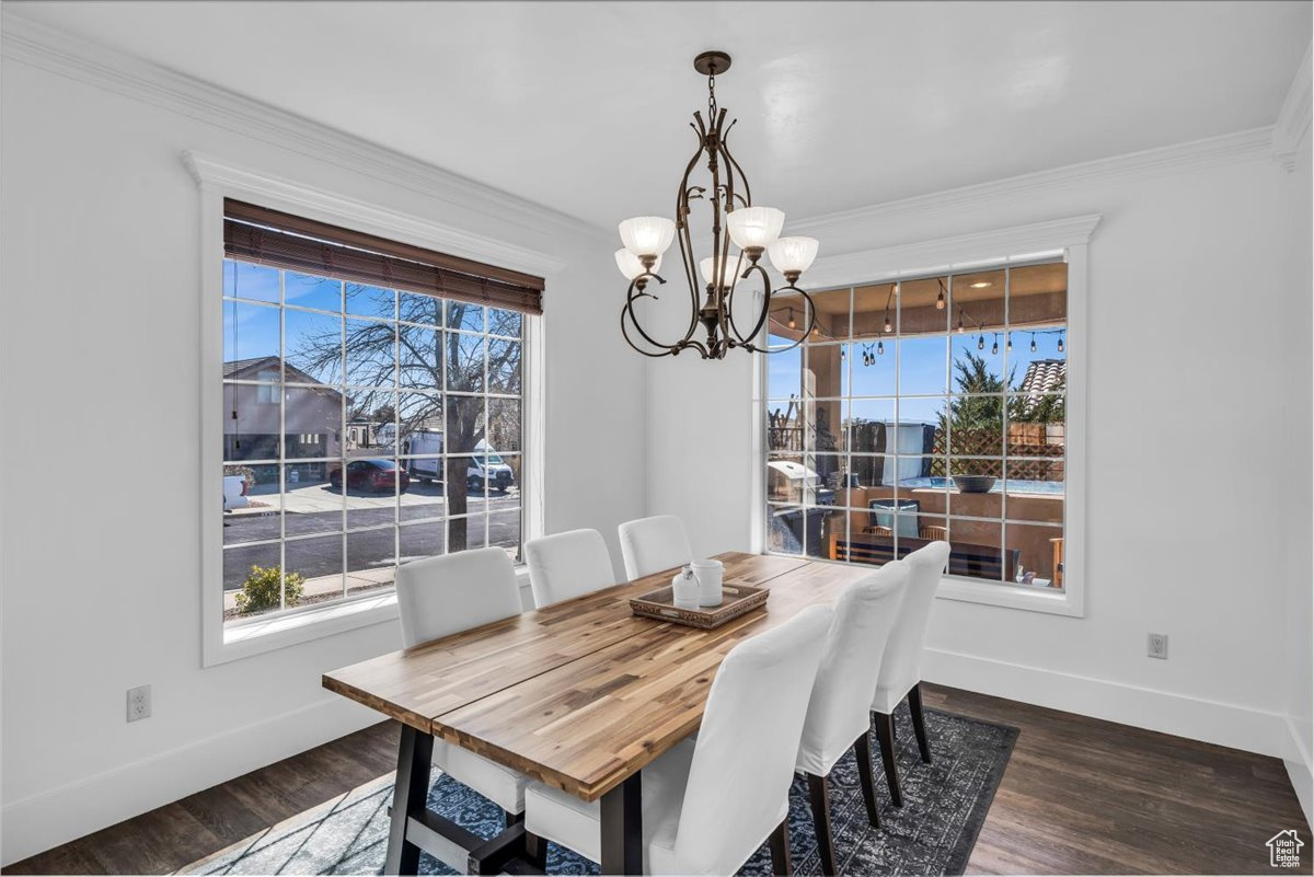 Dining area with ornamental molding, dark wood-type flooring, a notable chandelier, and baseboards