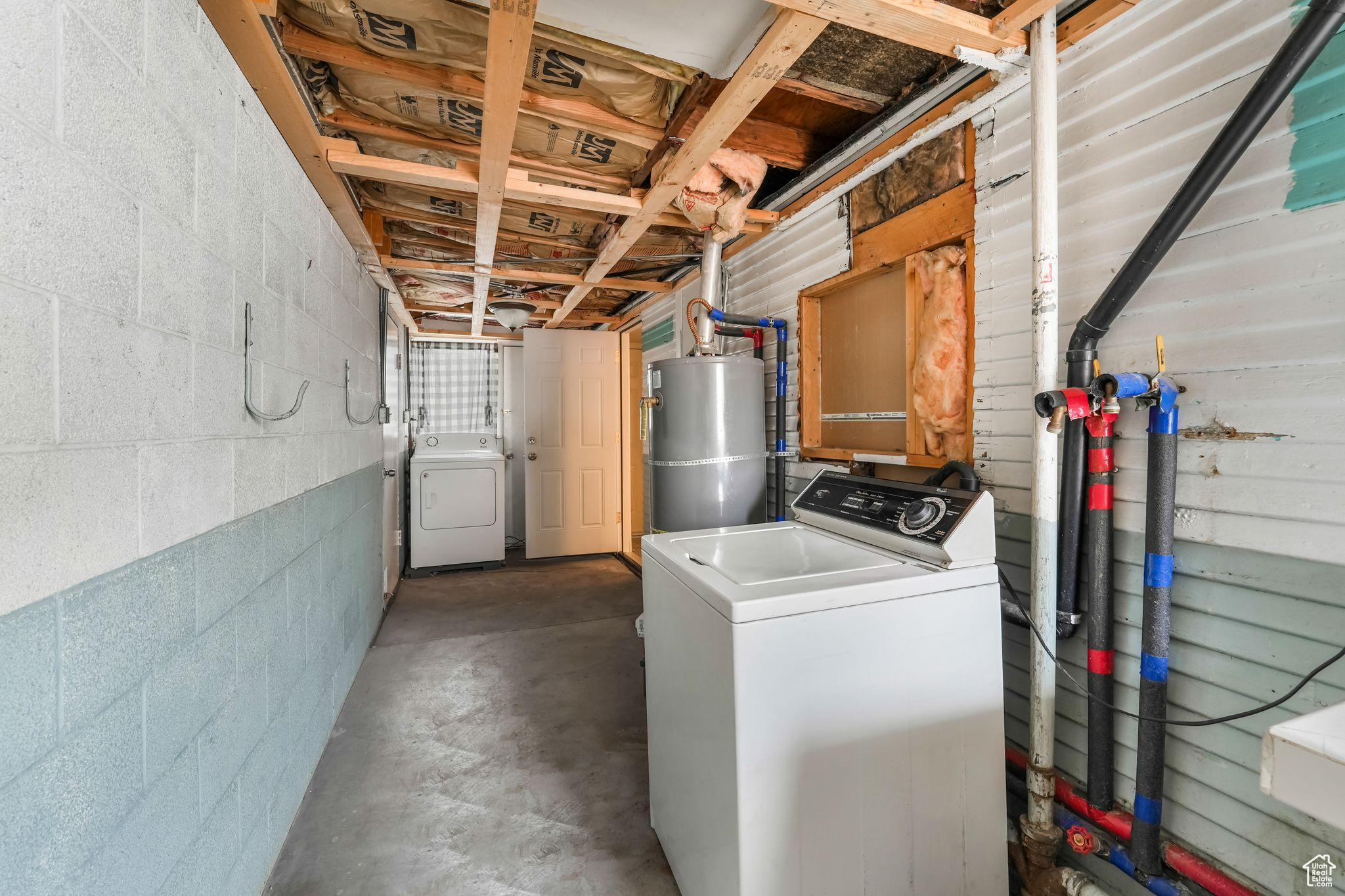 Unfinished below grade area with concrete block wall, strapped water heater, and washer / clothes dryer
