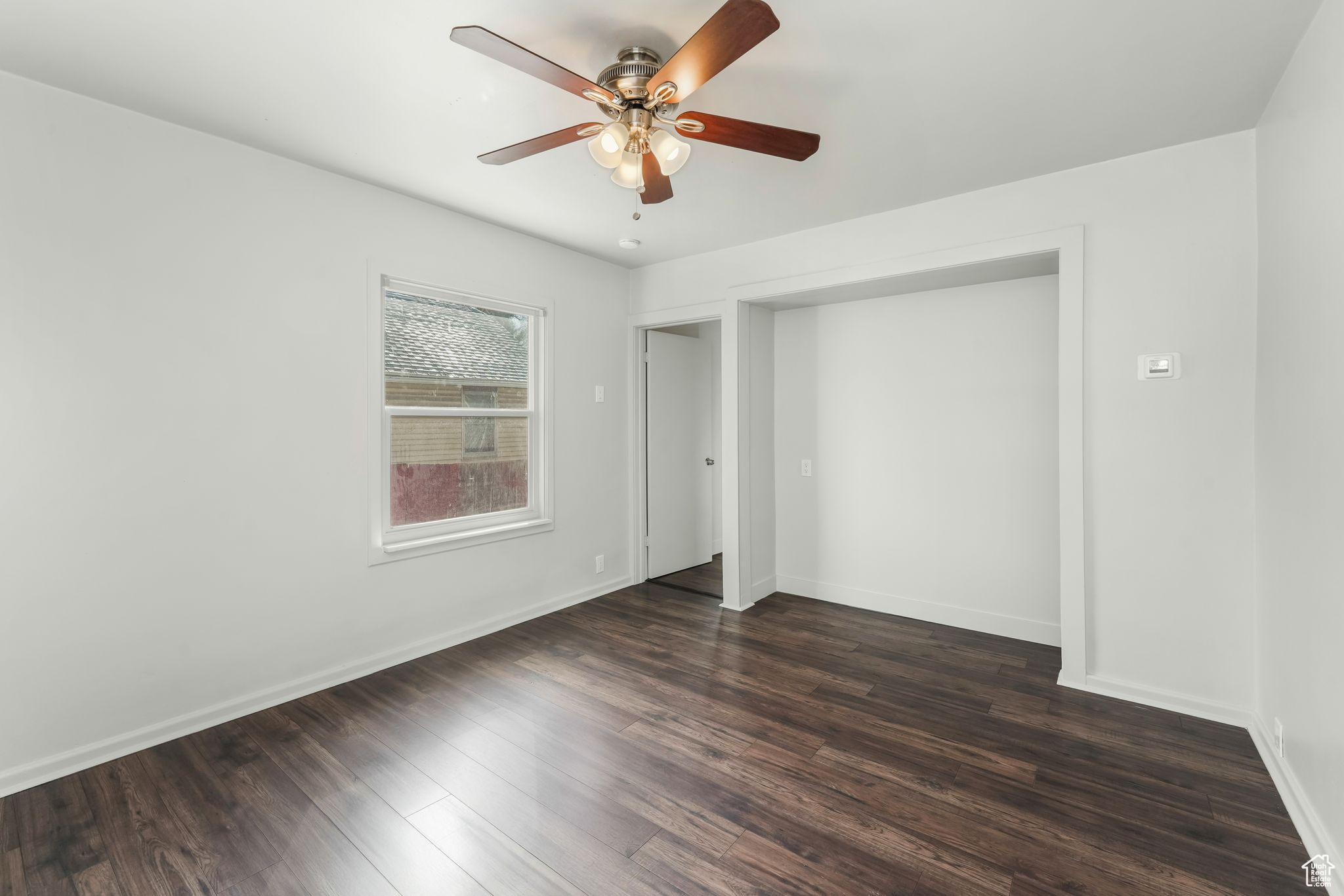 Unfurnished bedroom featuring dark wood-style flooring, a ceiling fan, and baseboards