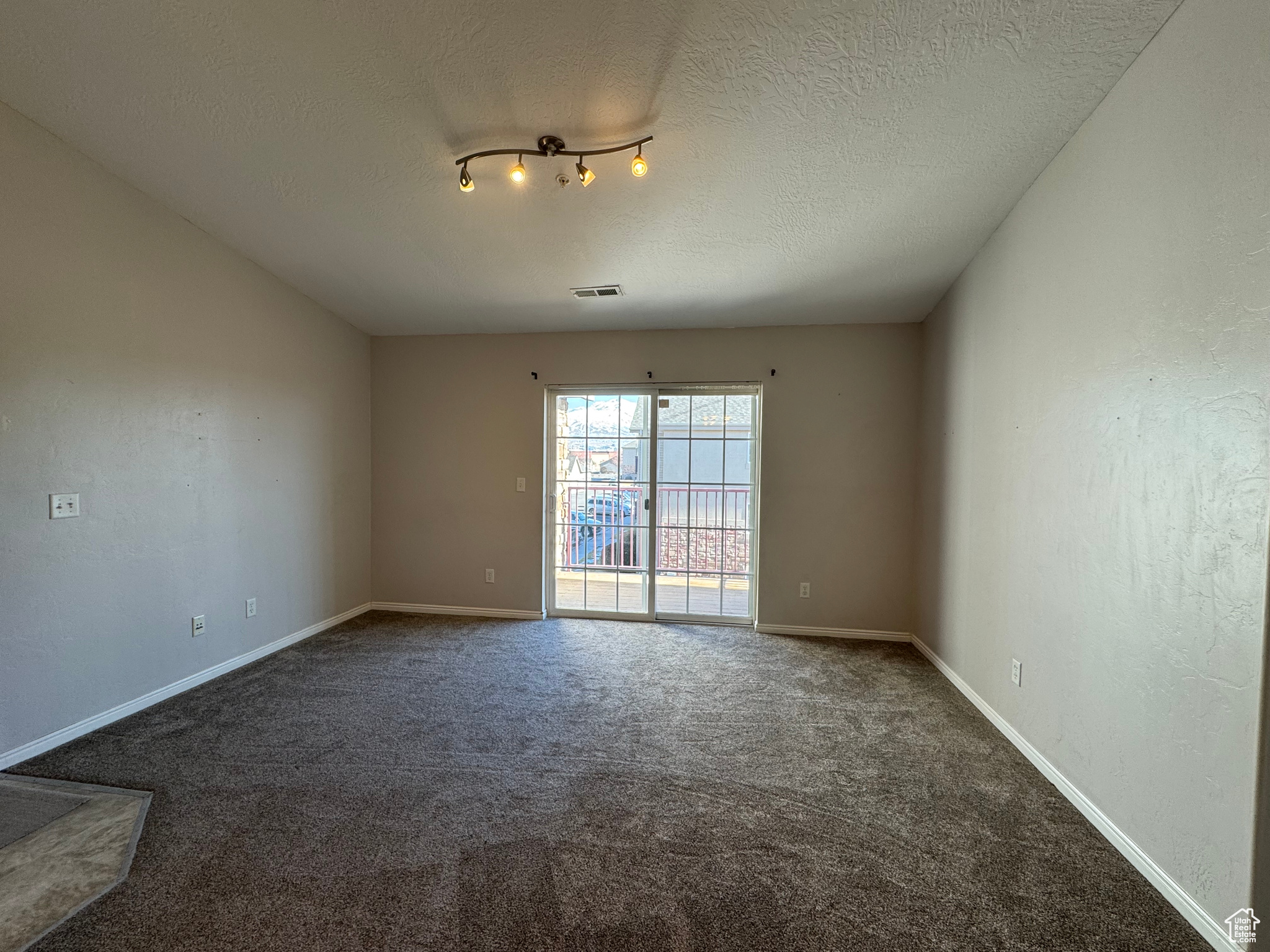 Empty room with a textured ceiling, carpet, visible vents, and baseboards