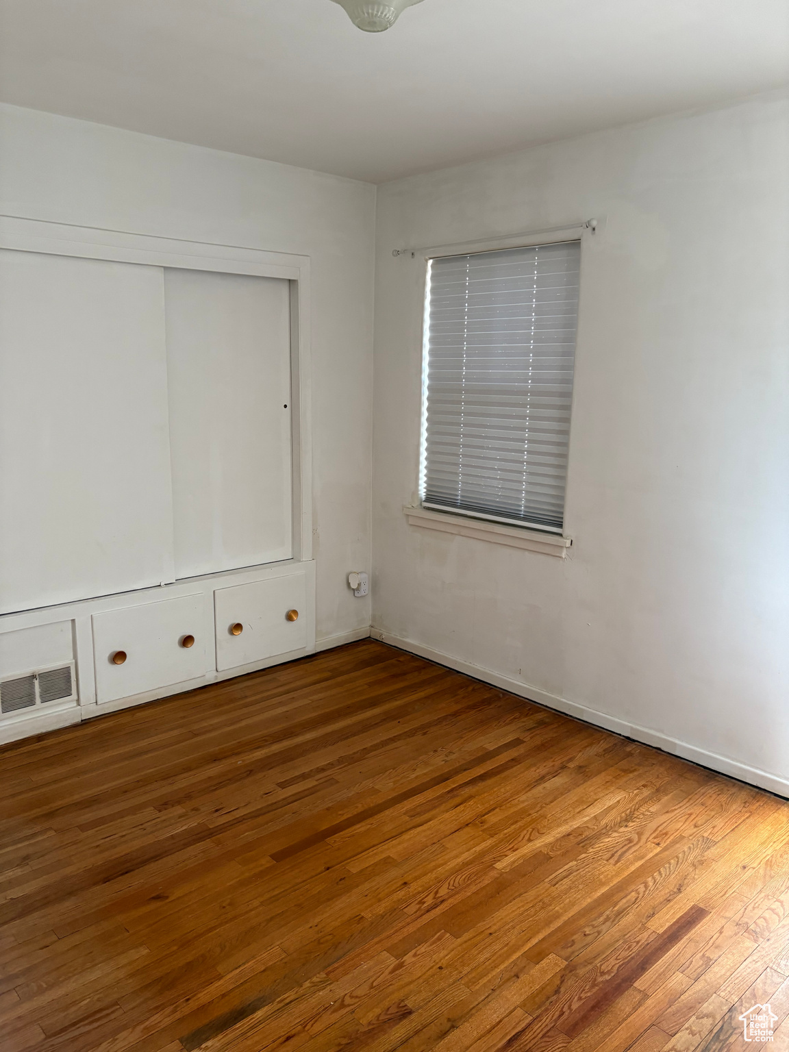 Unfurnished bedroom with hardwood / wood-style flooring, visible vents, and a closet