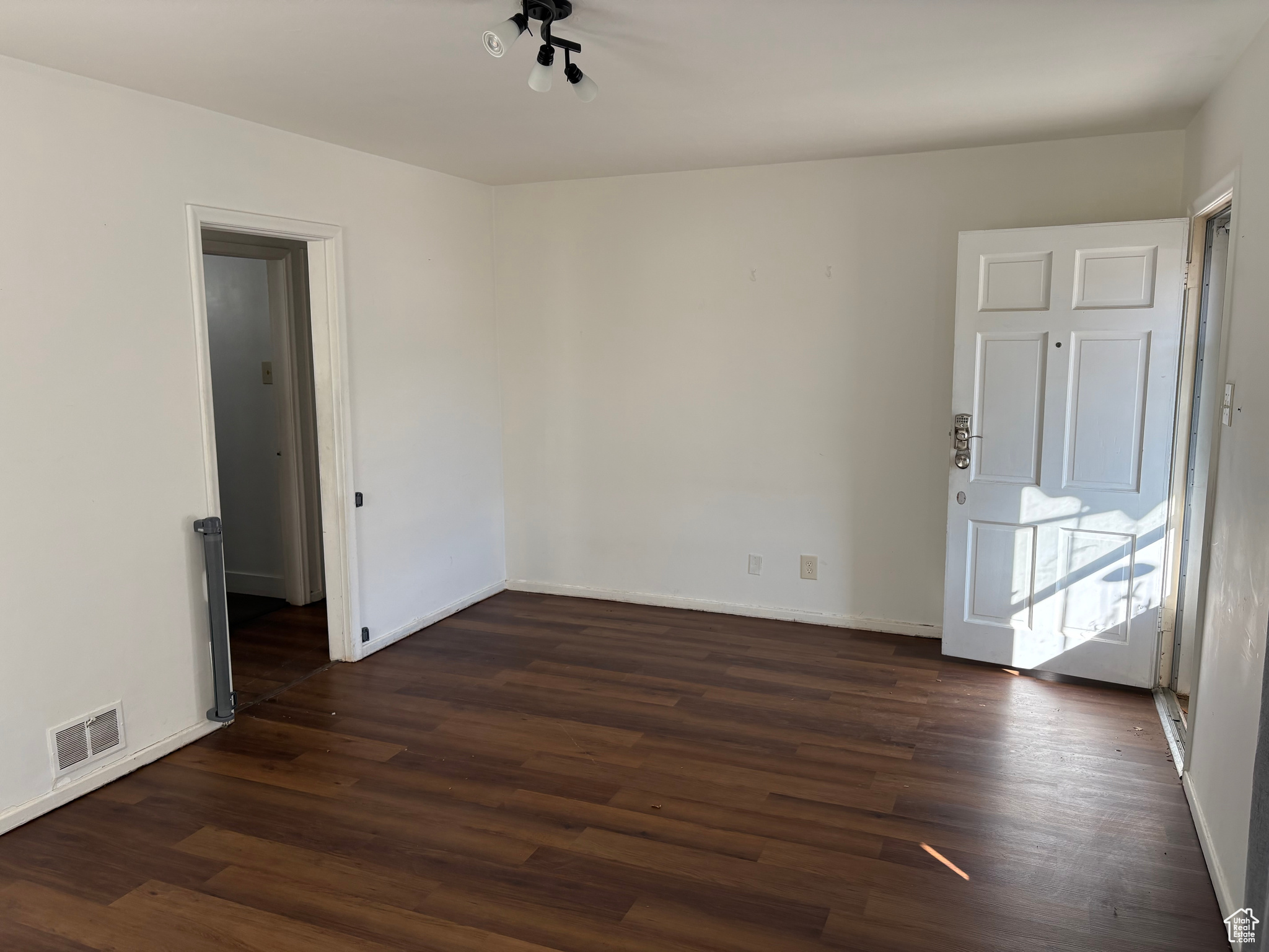 Unfurnished room featuring dark wood-style floors, visible vents, and baseboards