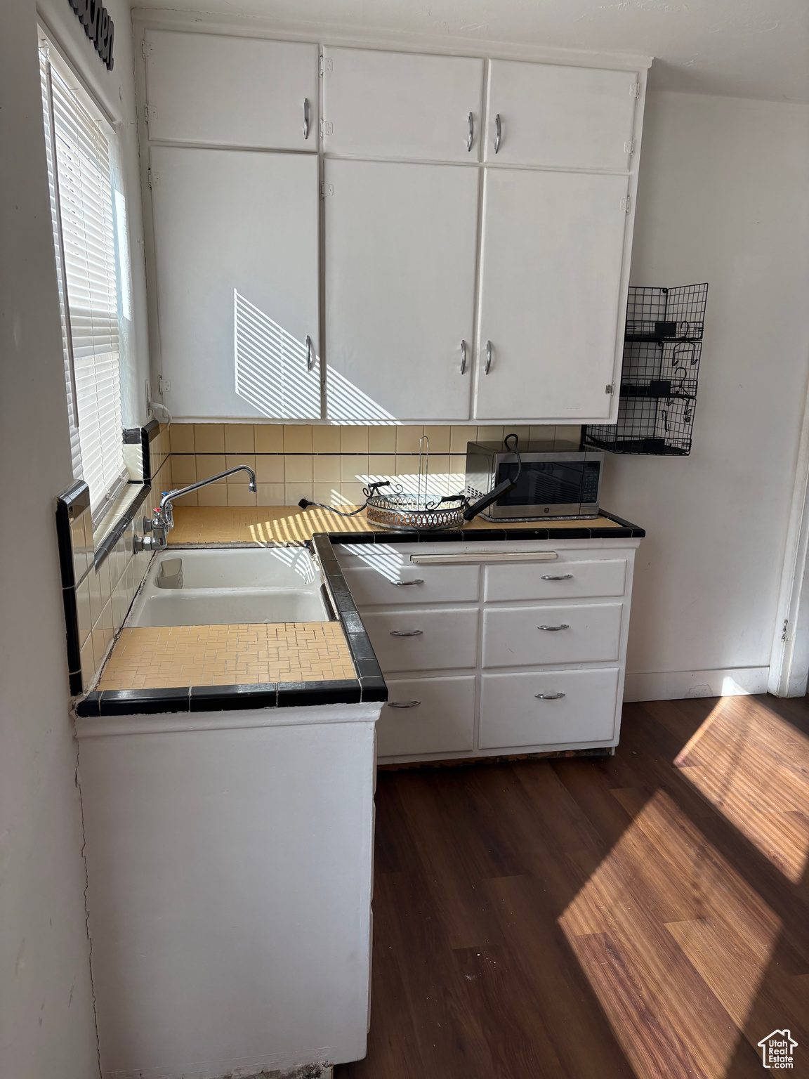 Kitchen with white cabinets, stainless steel microwave, dark wood-style flooring, a sink, and backsplash