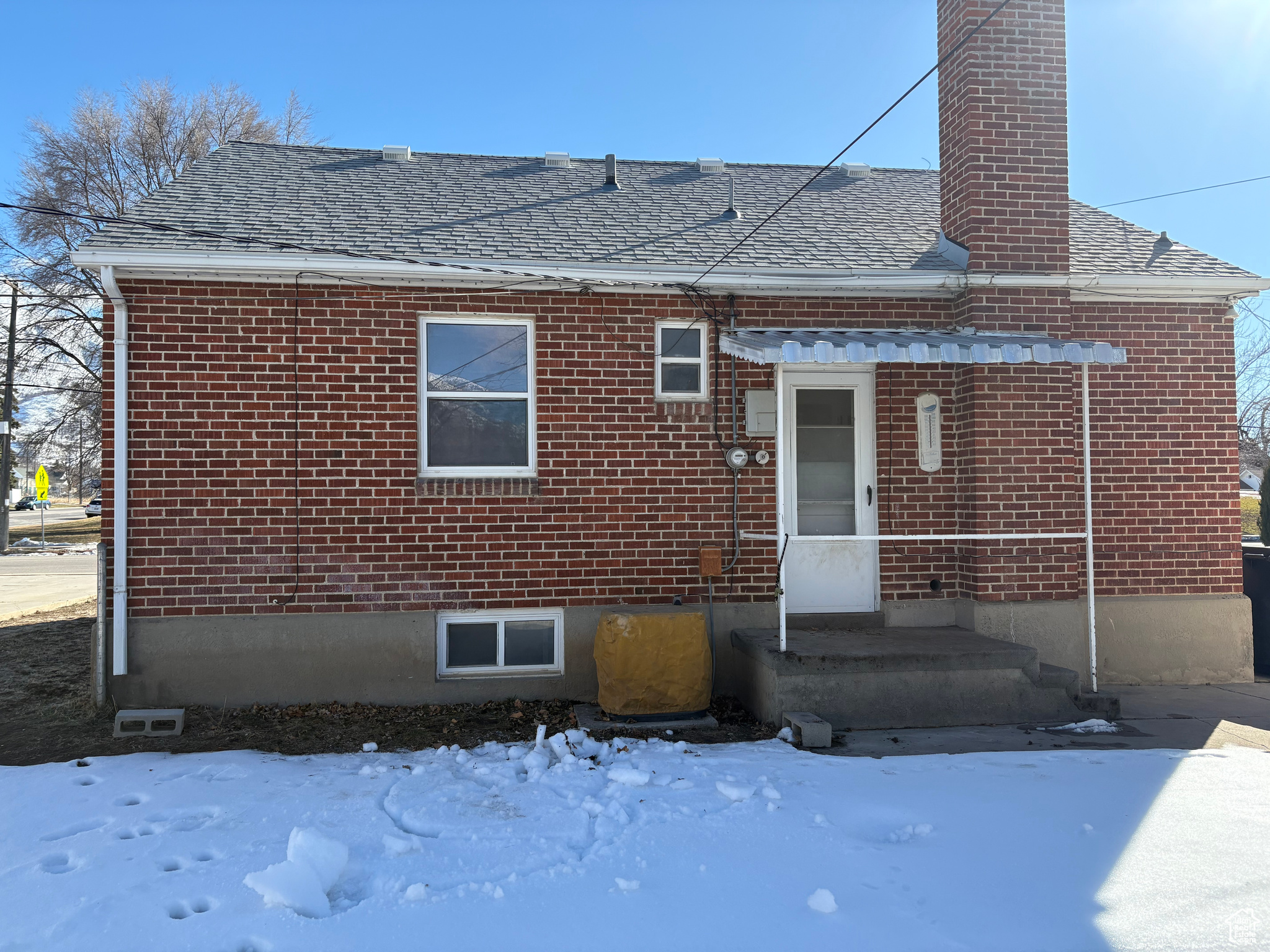 Exterior space featuring brick siding, a chimney, and roof with shingles
