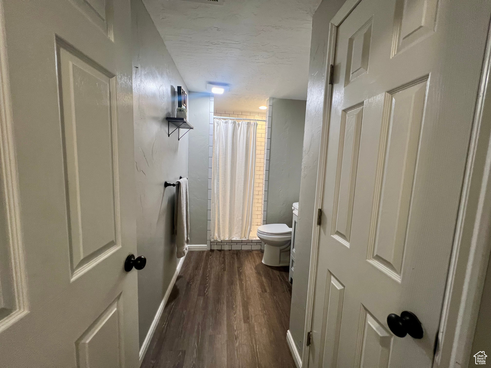 Bathroom with baseboards, a textured ceiling, toilet, and wood finished floors