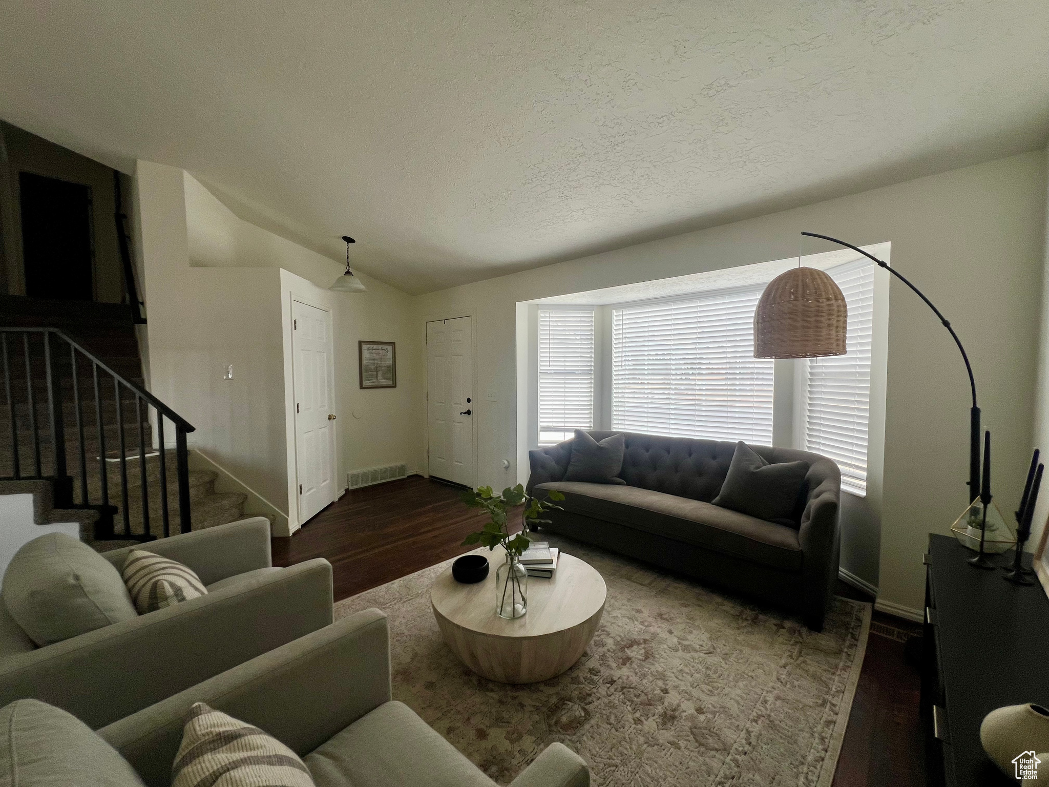 Living room with dark wood-type flooring, visible vents, vaulted ceiling, and stairs