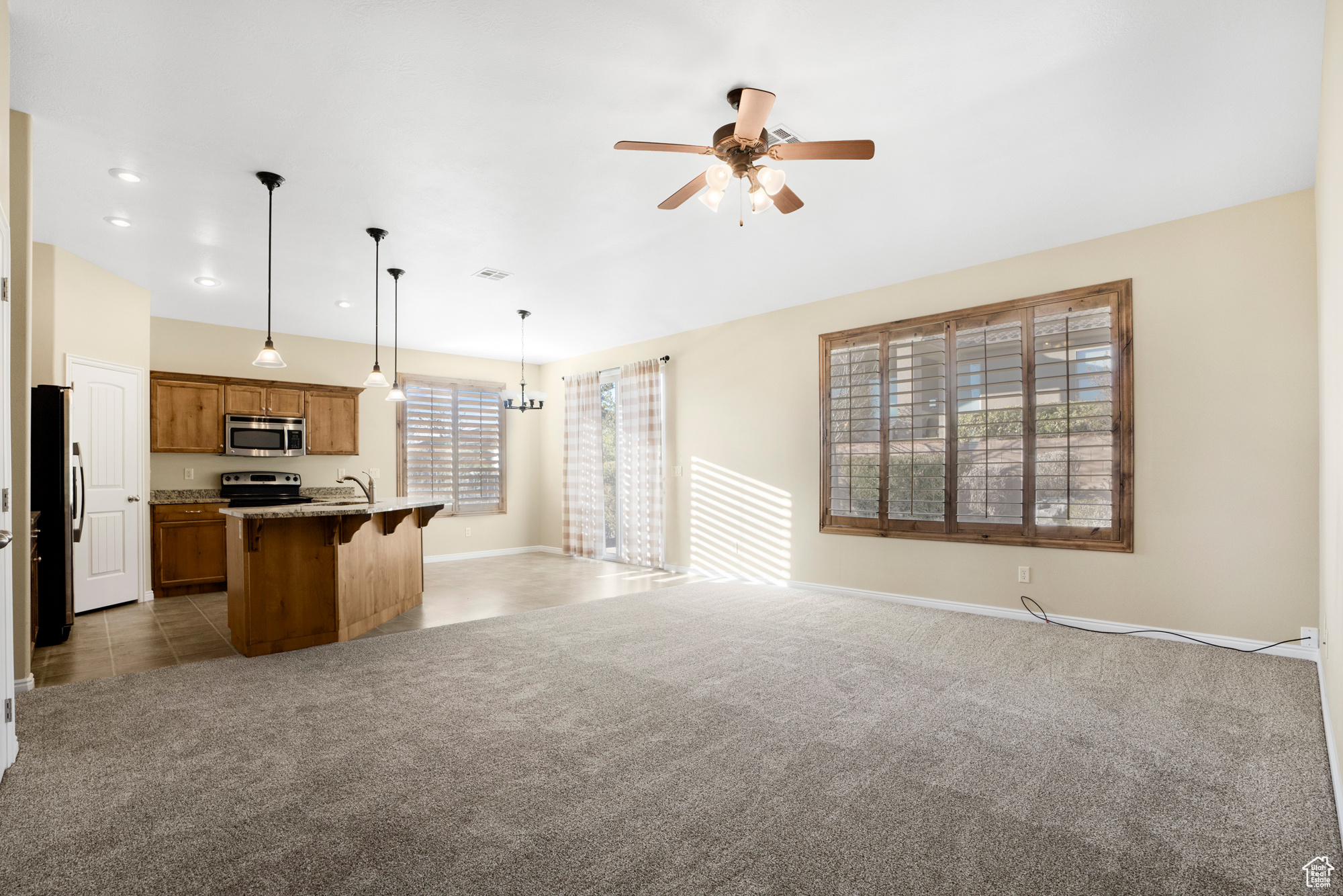 Kitchen with light carpet, an island with sink, open floor plan, hanging light fixtures, and stainless steel appliances