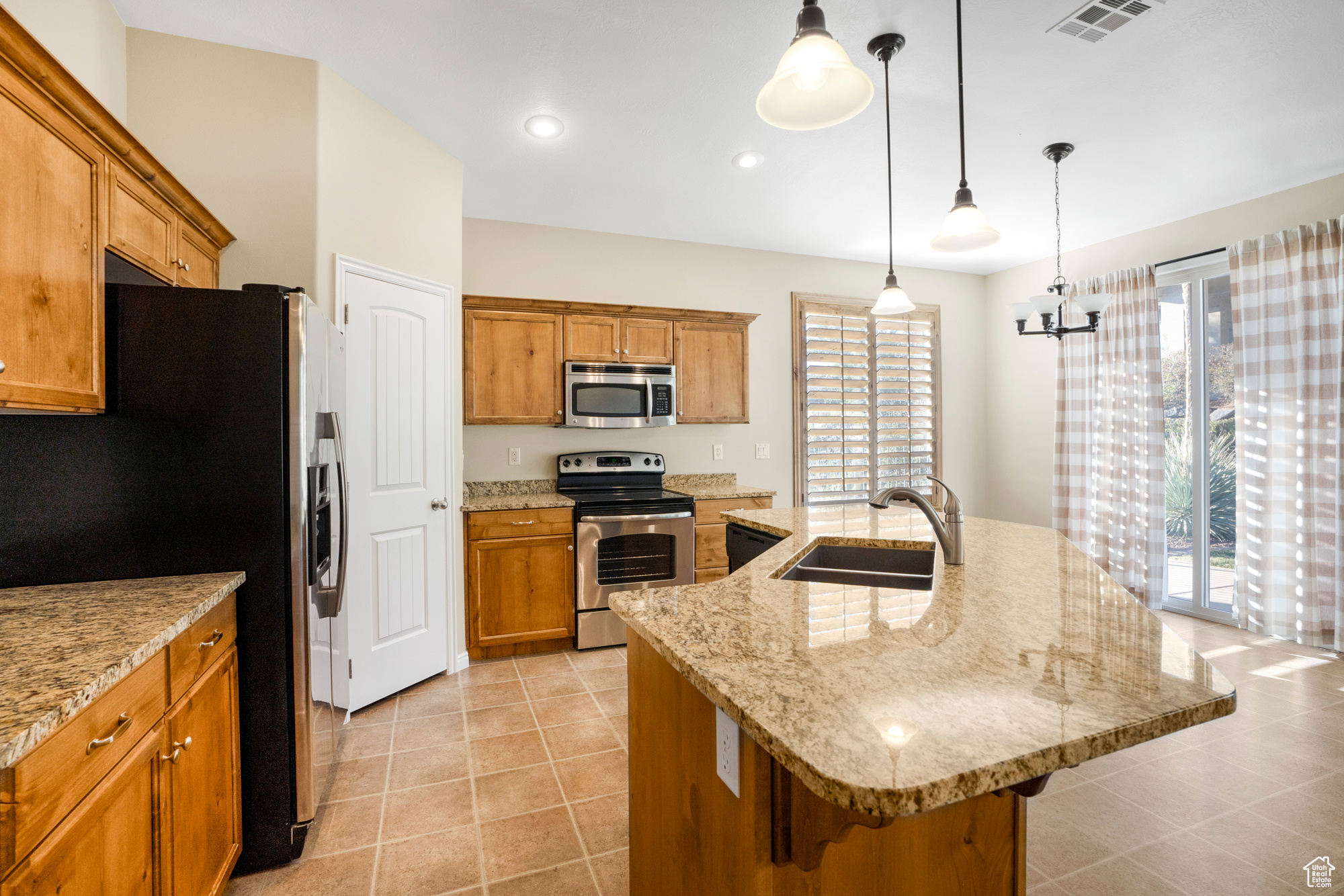 Kitchen featuring a center island with sink, visible vents, appliances with stainless steel finishes, pendant lighting, and a sink