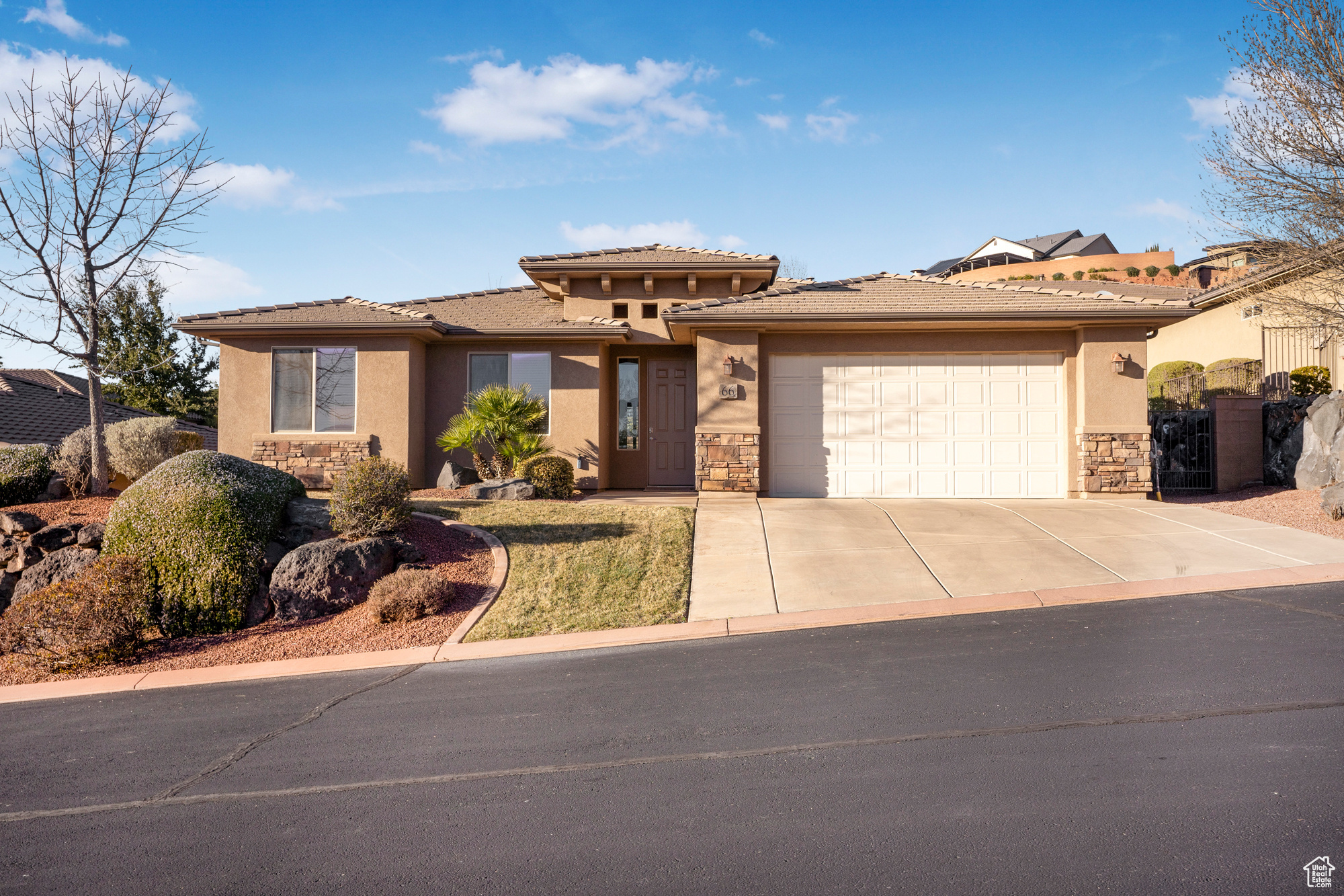 View of front facade featuring stucco siding, an attached garage, stone siding, driveway, and a tiled roof